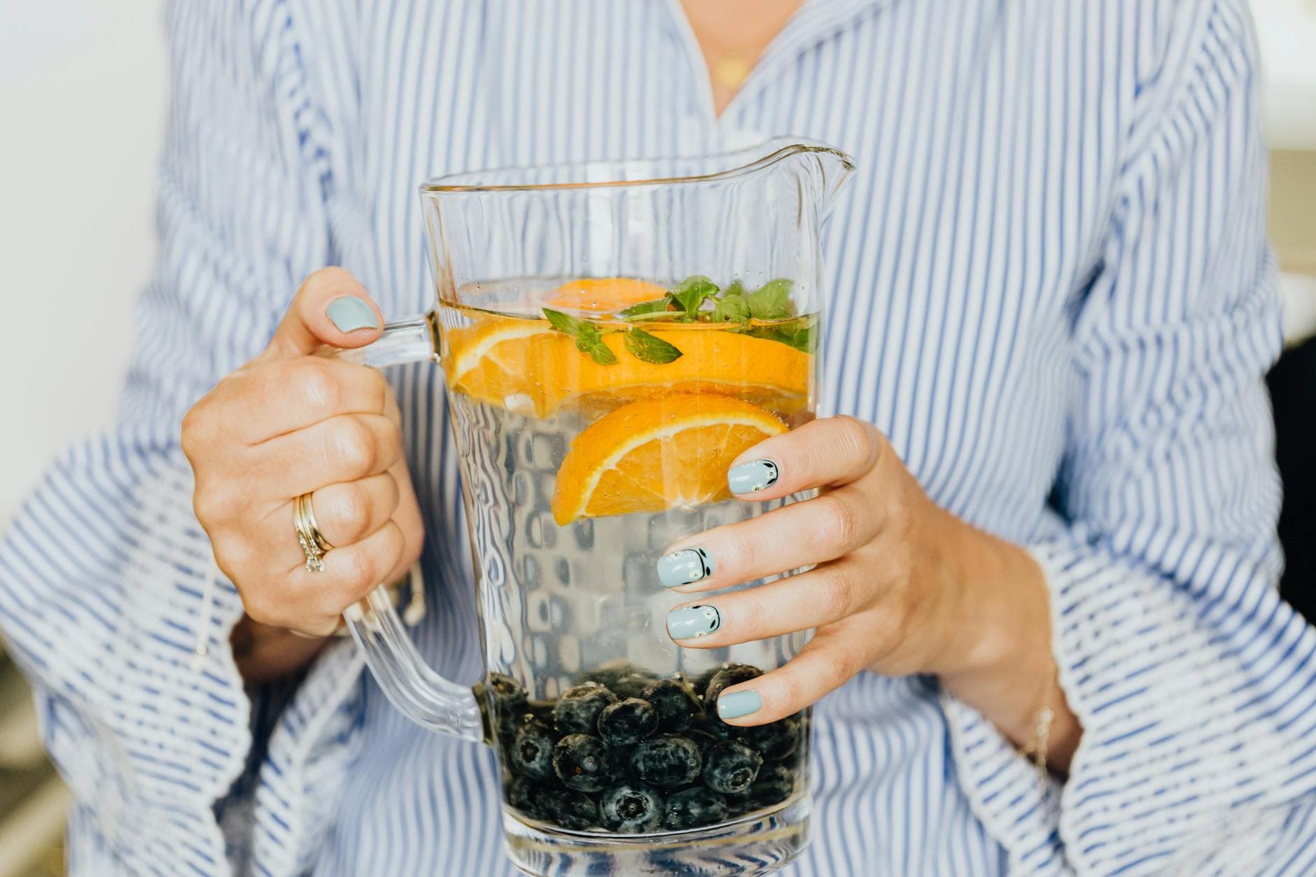 Close-up of infused water with oranges, blueberries, and mint in a glass pitcher. - detox water recipe