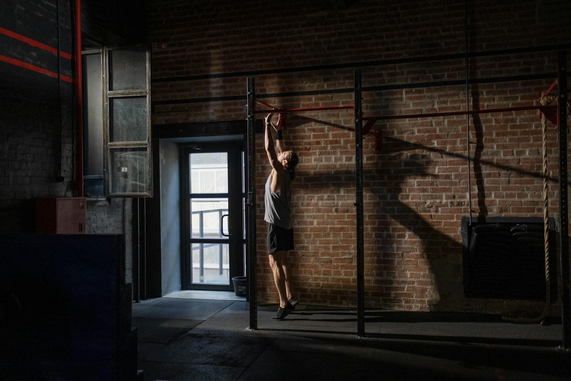 A man exercises on a pull-up bar in an industrial-style gym with brick walls, conveying fitness and dedication. - bodyweight cardio