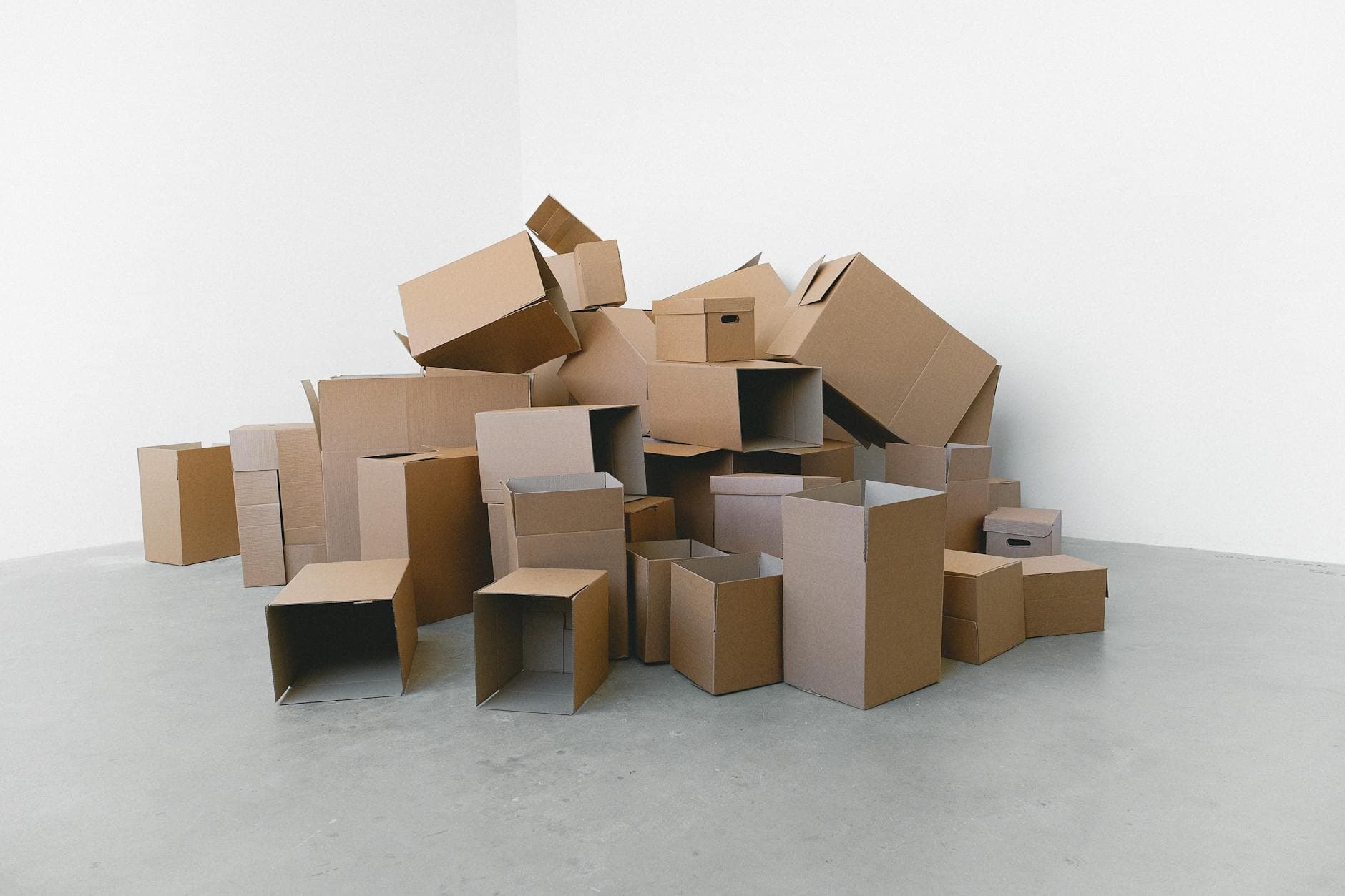 A pile of empty cardboard boxes arranged on a grey floor against a white wall, perfect for moving themes. - declutter diet habits