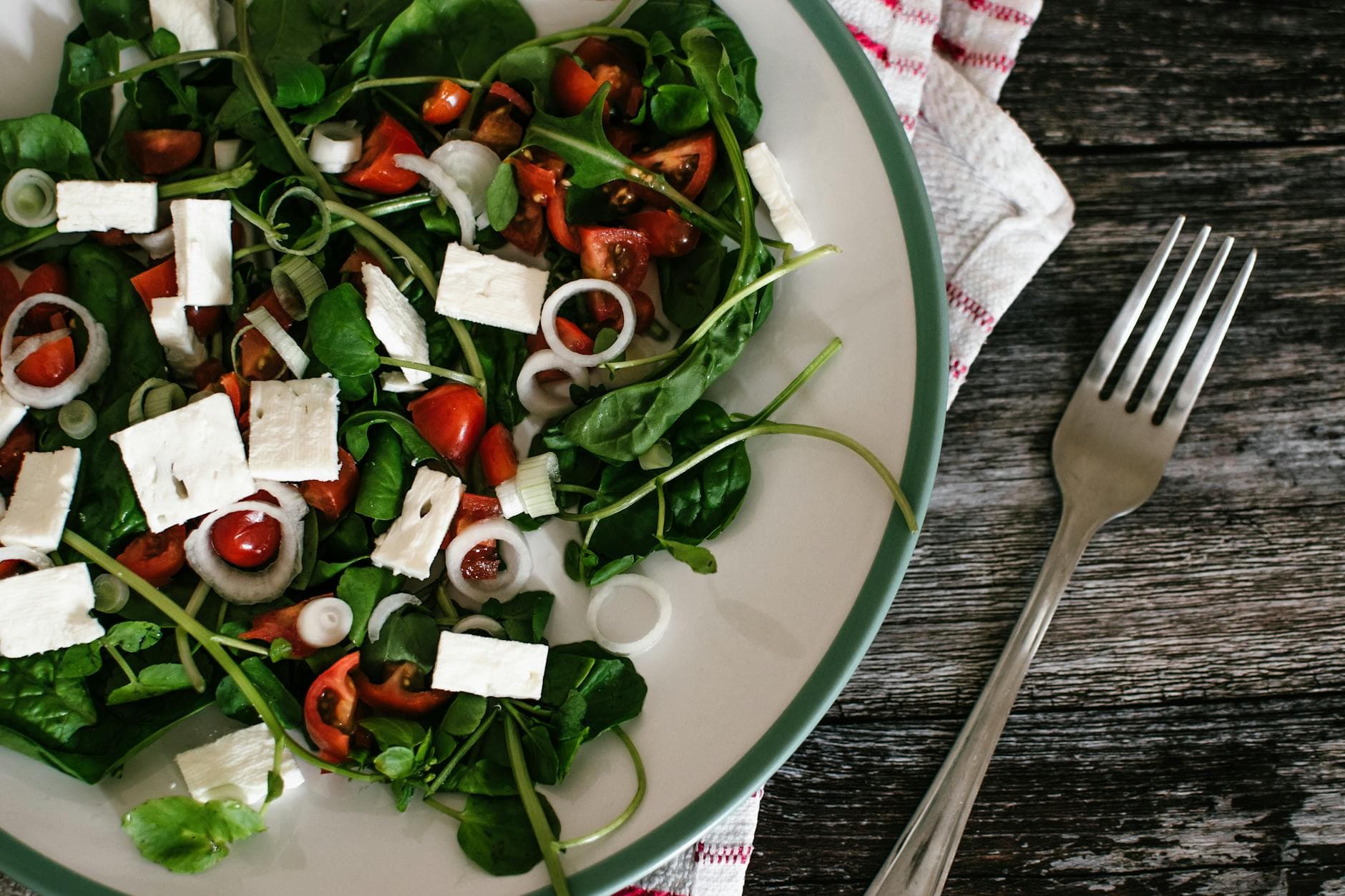 A vibrant and colorful spinach salad with feta cheese and tomatoes on a rustic table. - healthy kids lunches