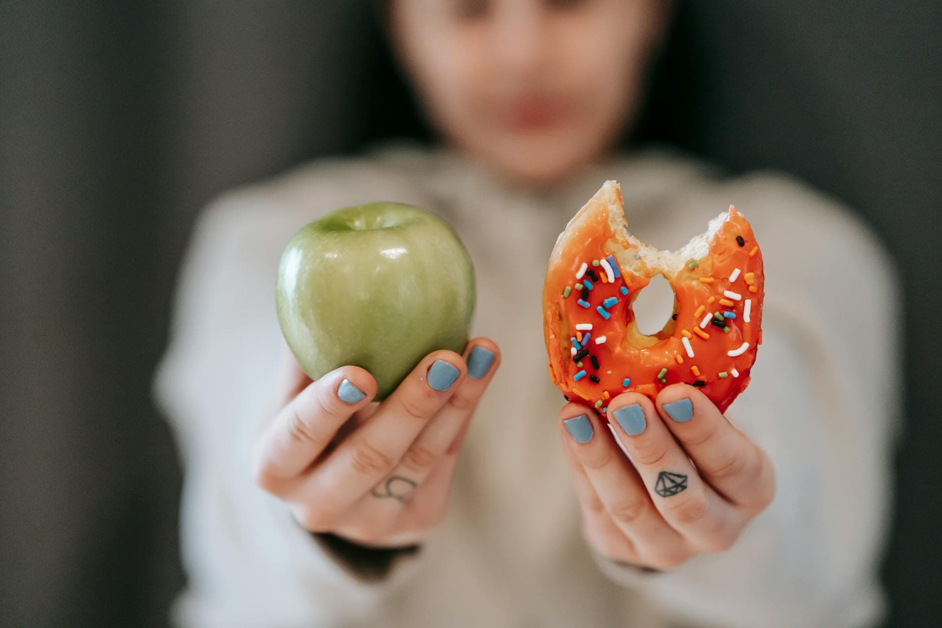 A close-up of a person holding an apple and a donut, symbolizing the choice between healthy eating and indulgence. - healthy sweet snacks