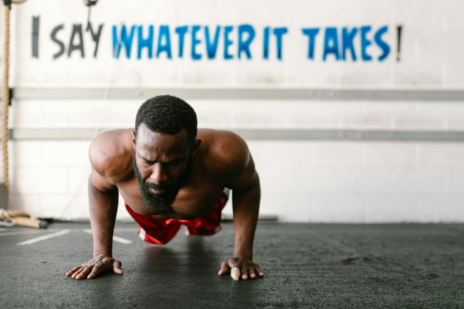 A man in a gym doing push-ups with a motivational quote on the wall behind him. - hiit fat loss
