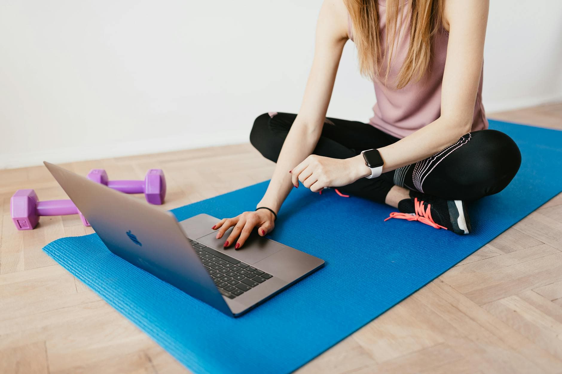 Woman in activewear using a laptop on a yoga mat with dumbbells, representing a healthy lifestyle. - home fat burning workout