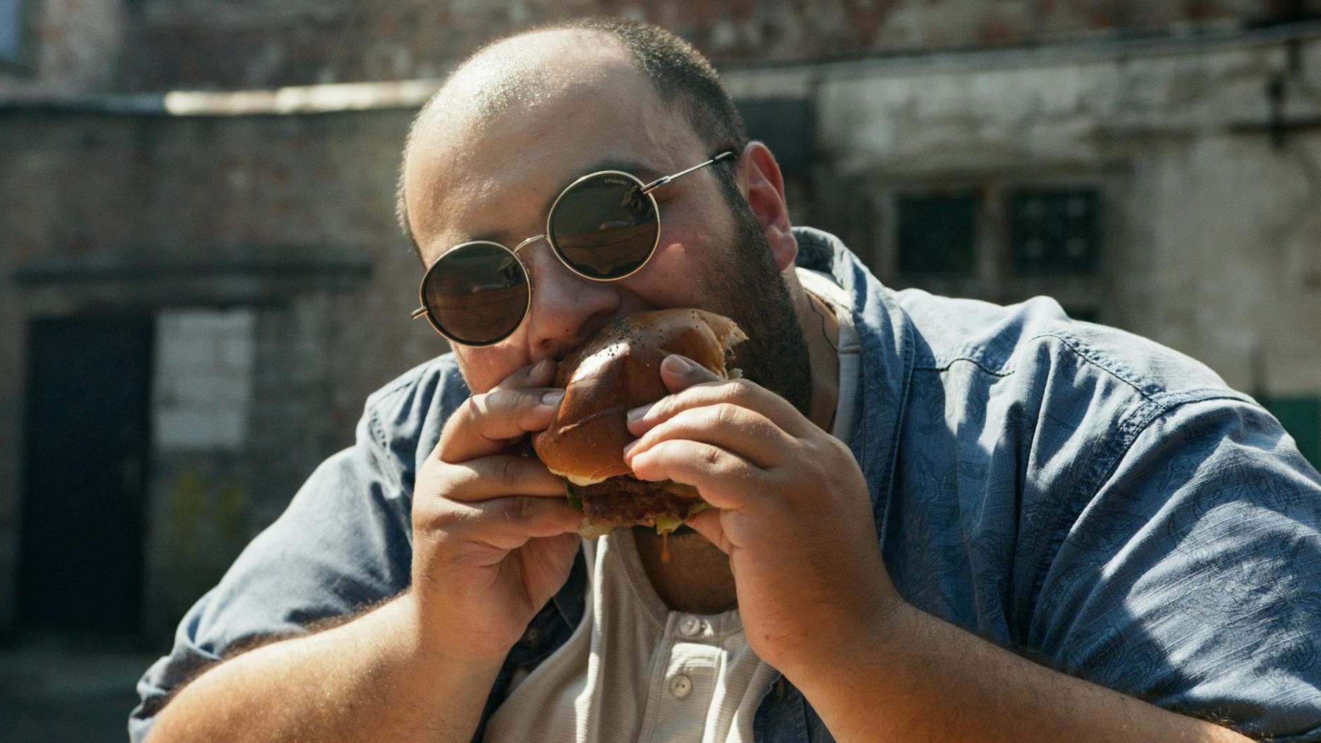 A man wearing sunglasses enjoys a big burger outdoors in London. - intermittent fasting weight loss