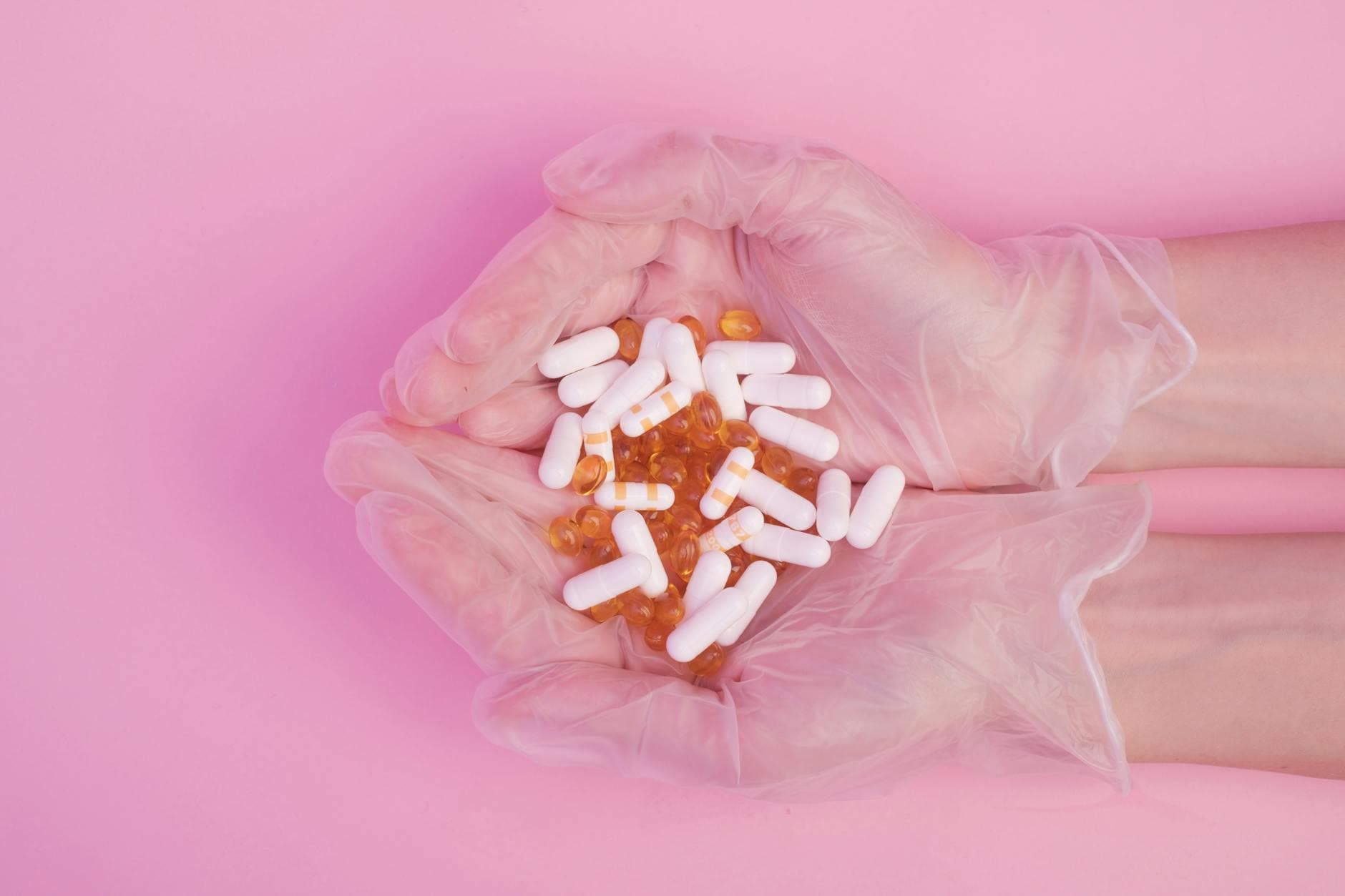 From above crop anonymous female in sterile medical gloves with handful of various medicine capsules against pink background - probiotics benefits