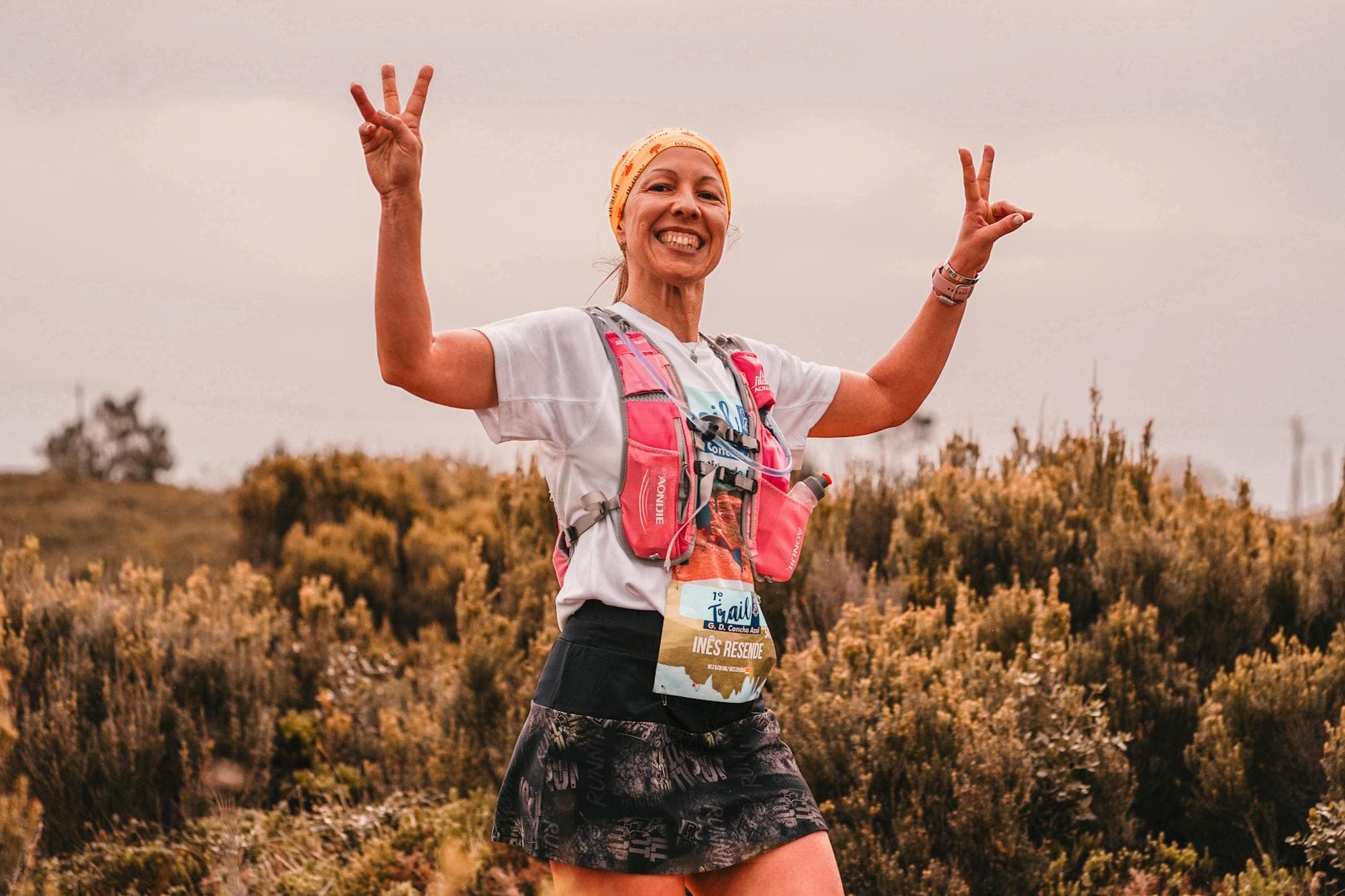 Smiling female athlete on a nature trail, celebrating with peace signs. - spring trail running