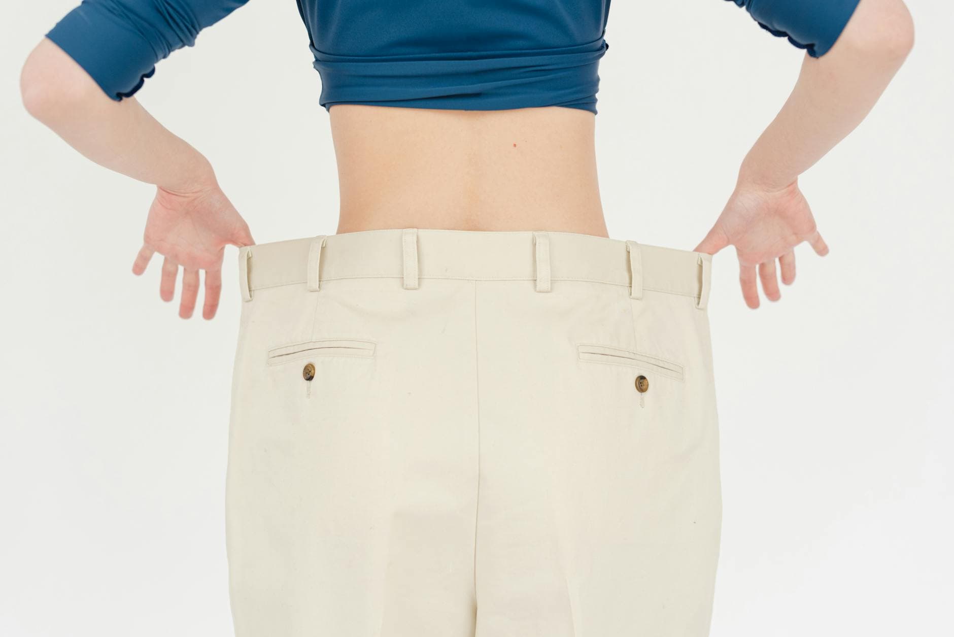 A woman's back view showcasing weight loss with oversized pants in a studio setting. - weight loss men