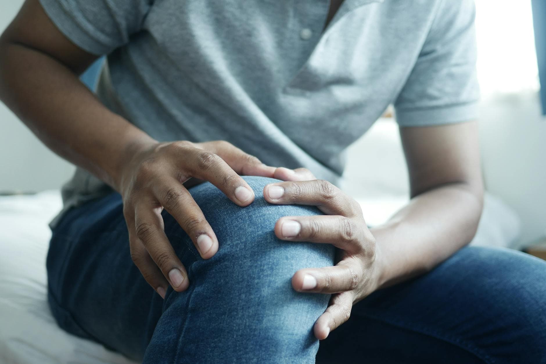 Close-up of a man holding his knee, capturing a moment of discomfort in a casual indoor setting. - back pain causes