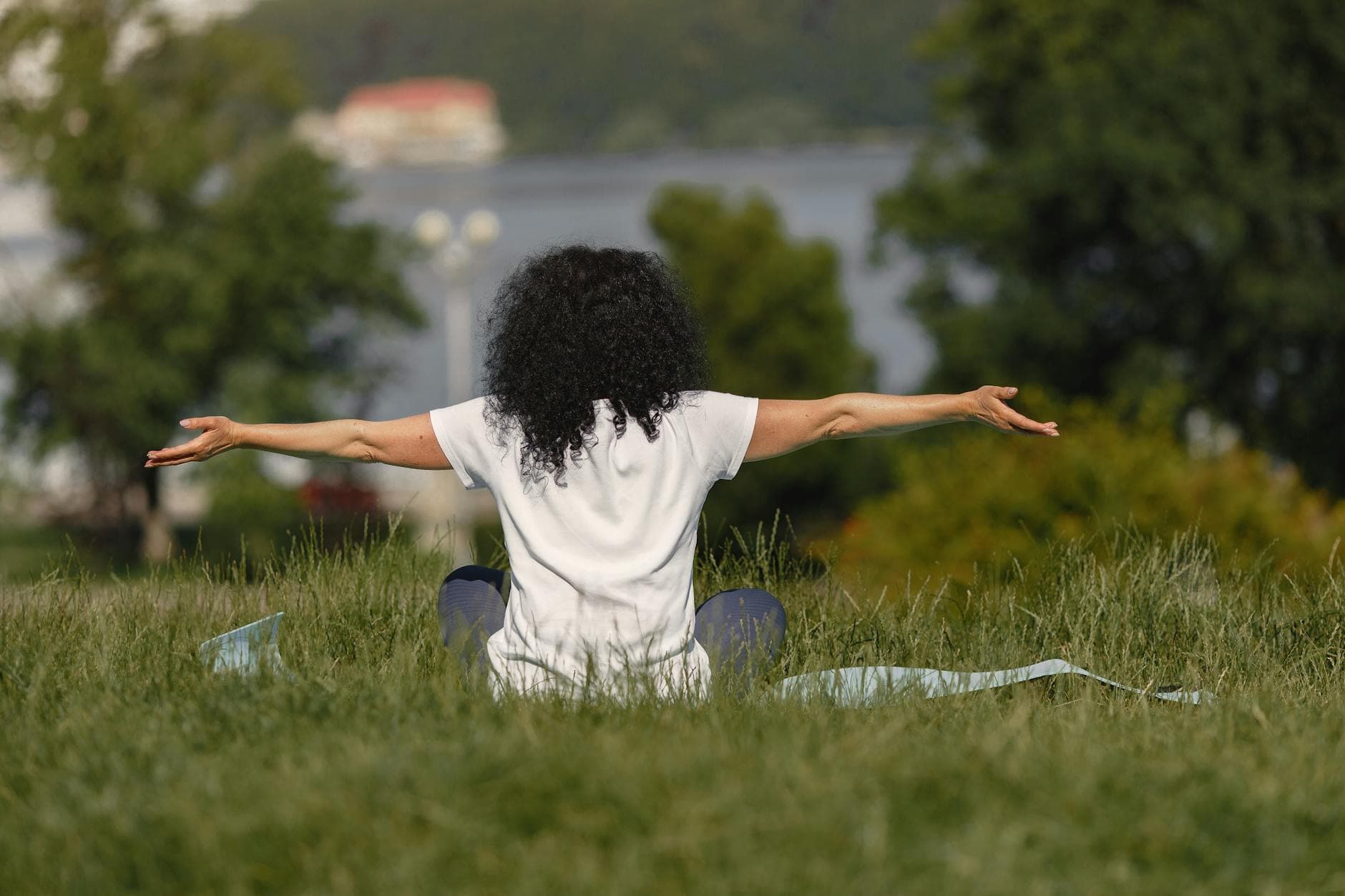 A woman with curly hair practices yoga on a mat in a grassy field by the water. - gentle yoga spring