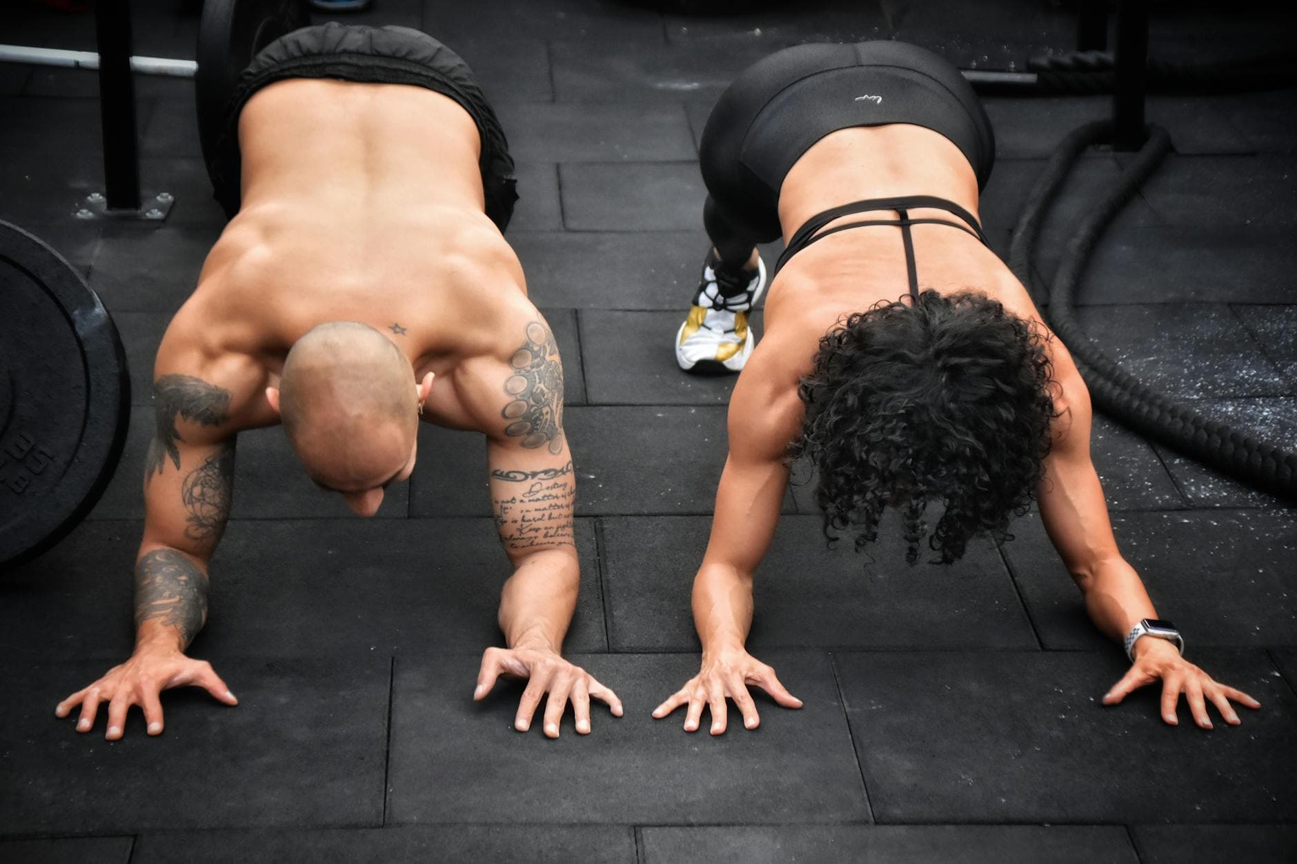Muscular tattooed man and woman doing push-ups in a gym setting, showcasing fitness strength. - hiit for busy people