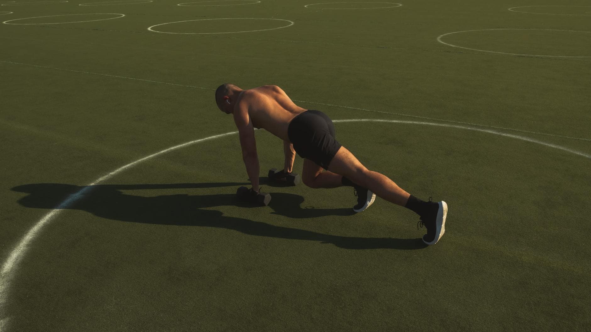 A fit man exercises shirtless with dumbbells in an outdoor field, showcasing fitness and strength. - hiit workout plan