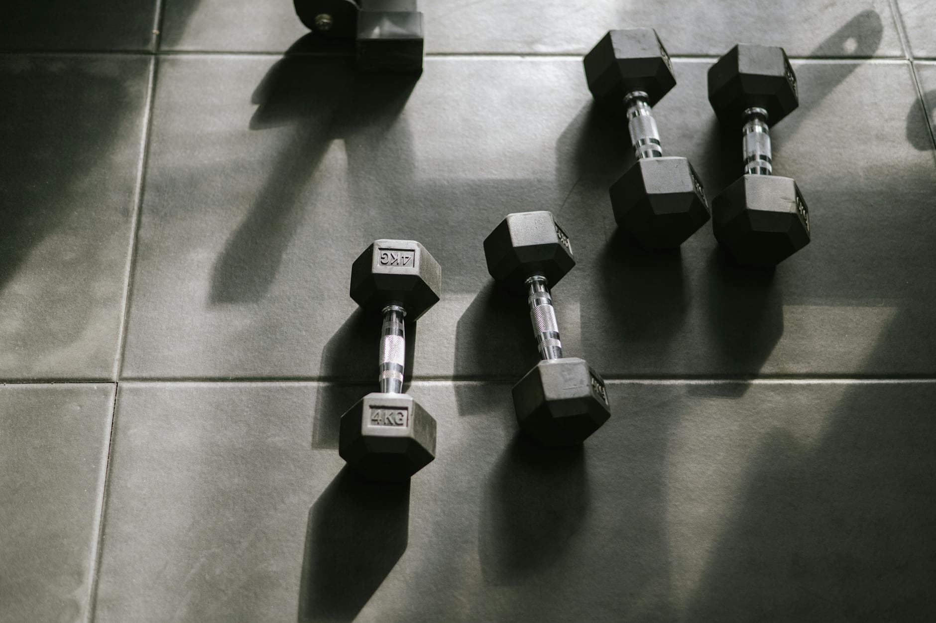 Hexagonal dumbbells on a gym floor bathed in natural sunlight, creating dynamic shadows. - at home strength