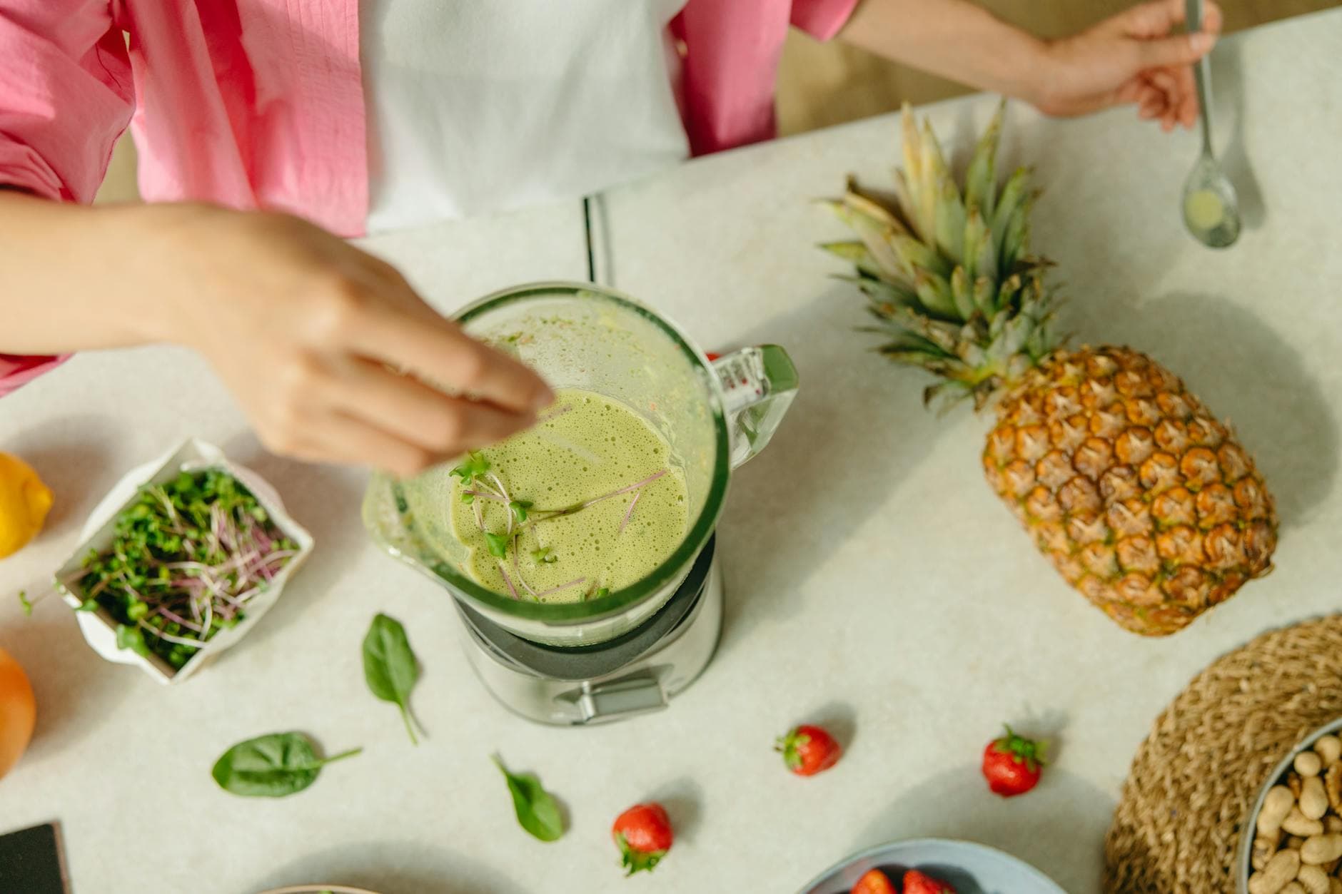 Top view of a green smoothie being prepared with pineapple and greens on a countertop. - mindful spring eating
