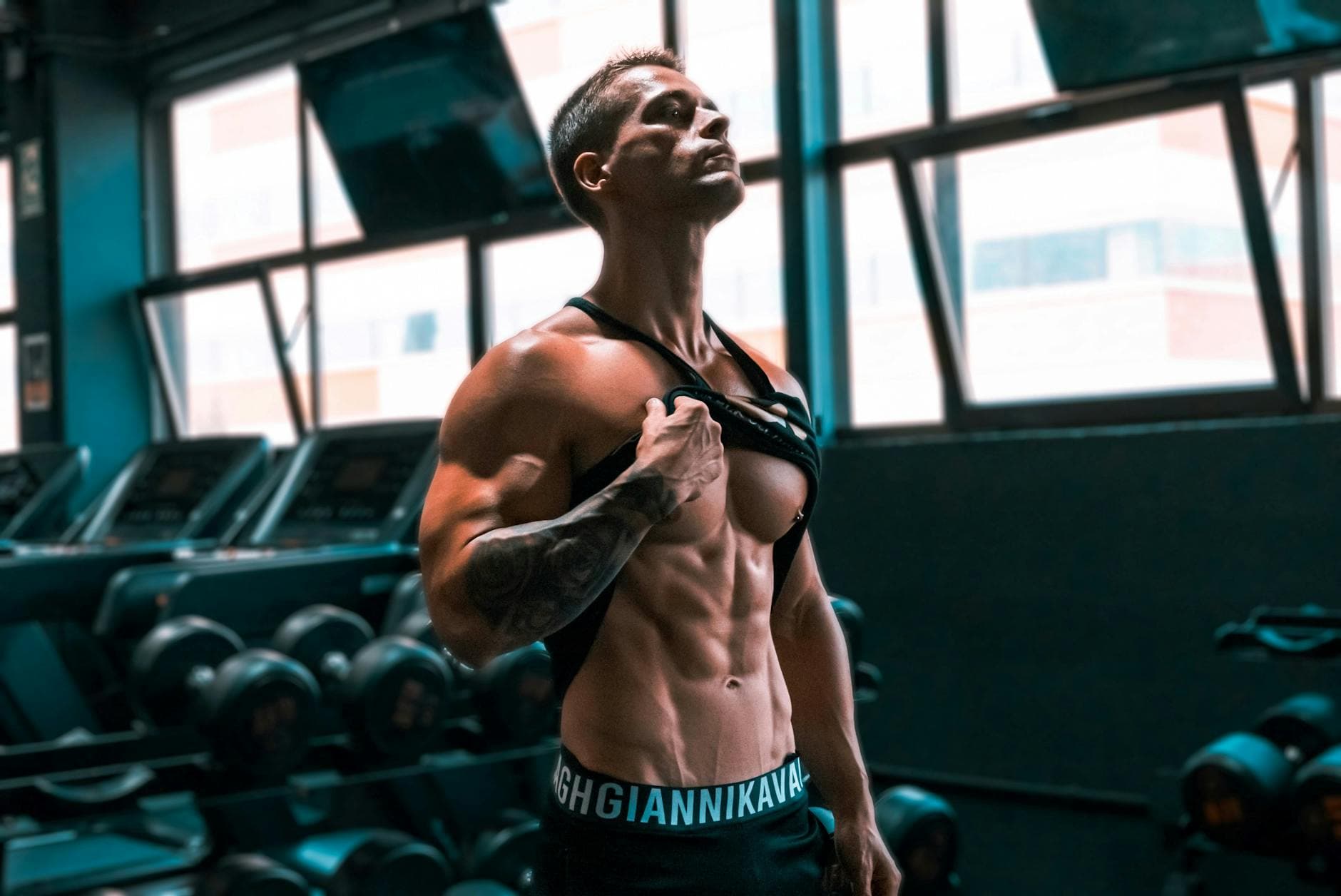Muscular man showing abs and tattoos in a gym setting. - muscular endurance exercises