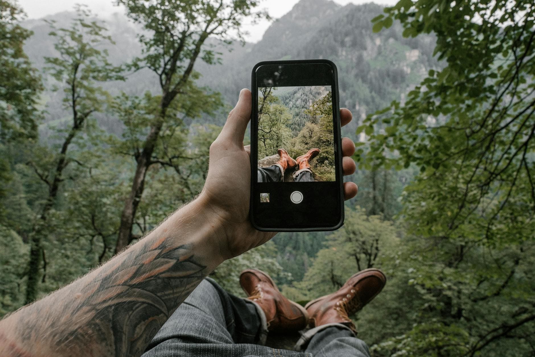 Person taking a smartphone photo of a scenic mountain view while relaxing outdoors. - nature digital detox
