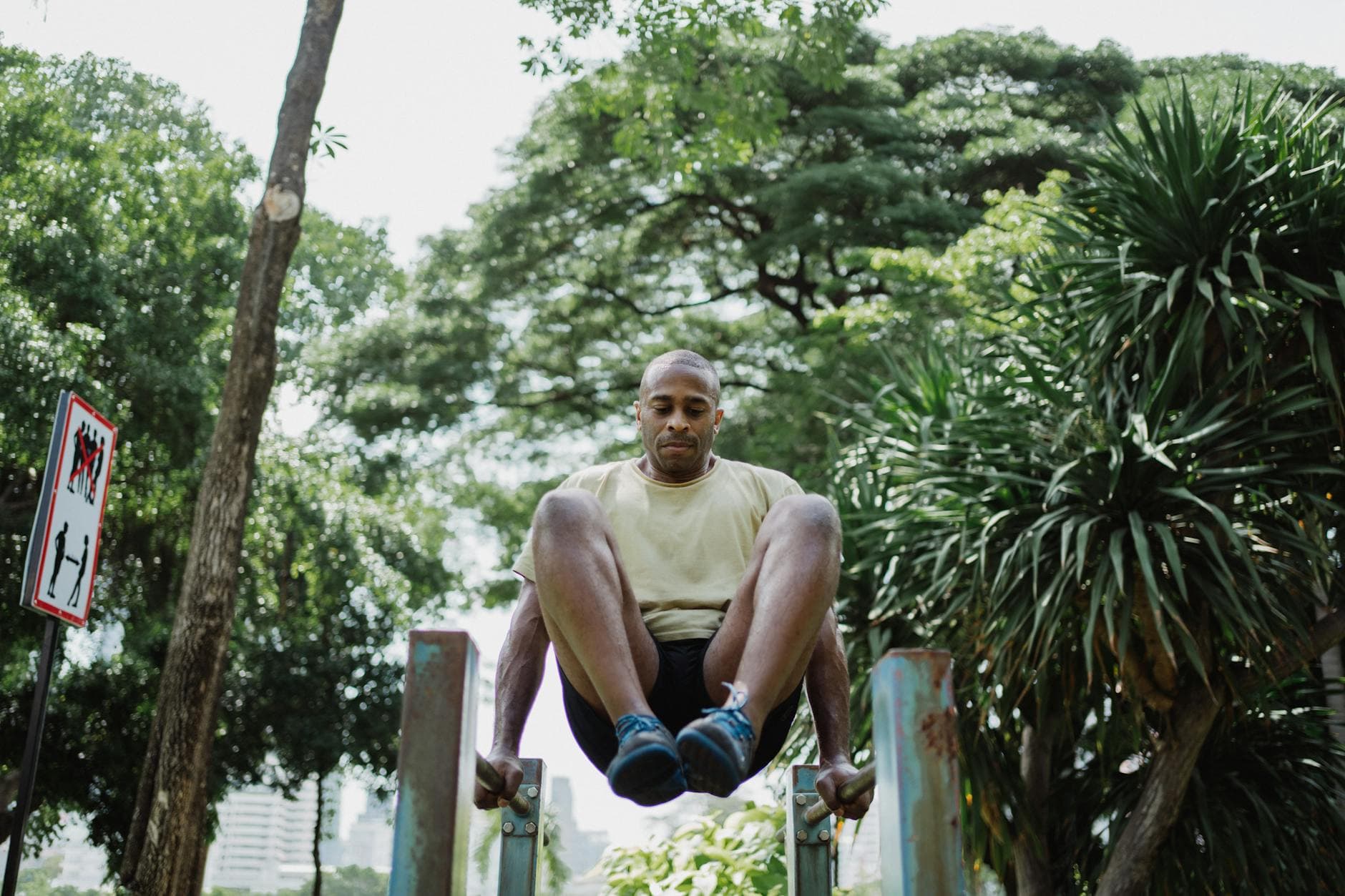 A man performs leg raises on a dip bar outdoors, surrounded by lush greenery. - outdoor hiit workouts