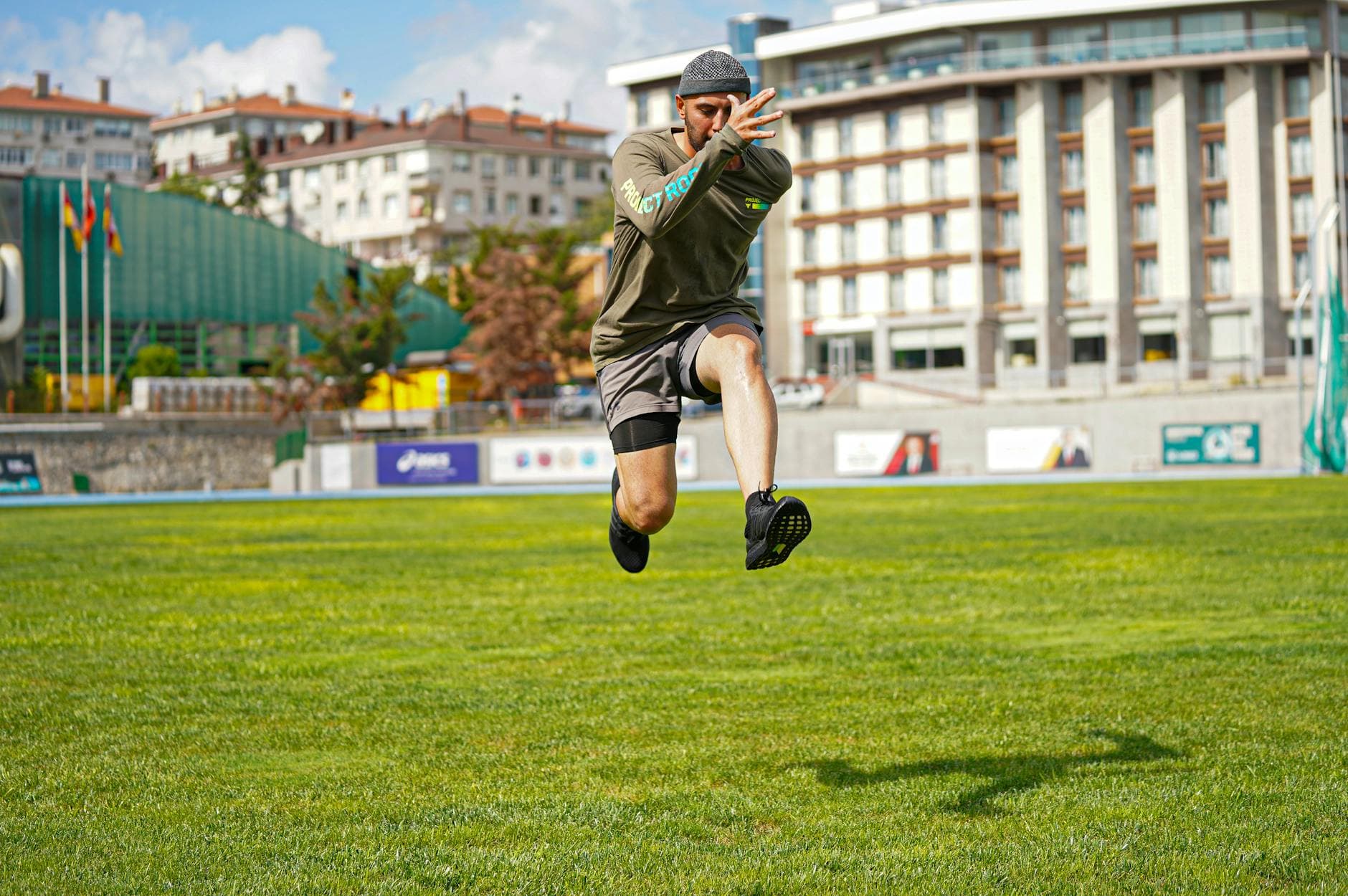 Energetic action photo of a man jumping on a grassy field in a cityscape background. - outdoor interval training
