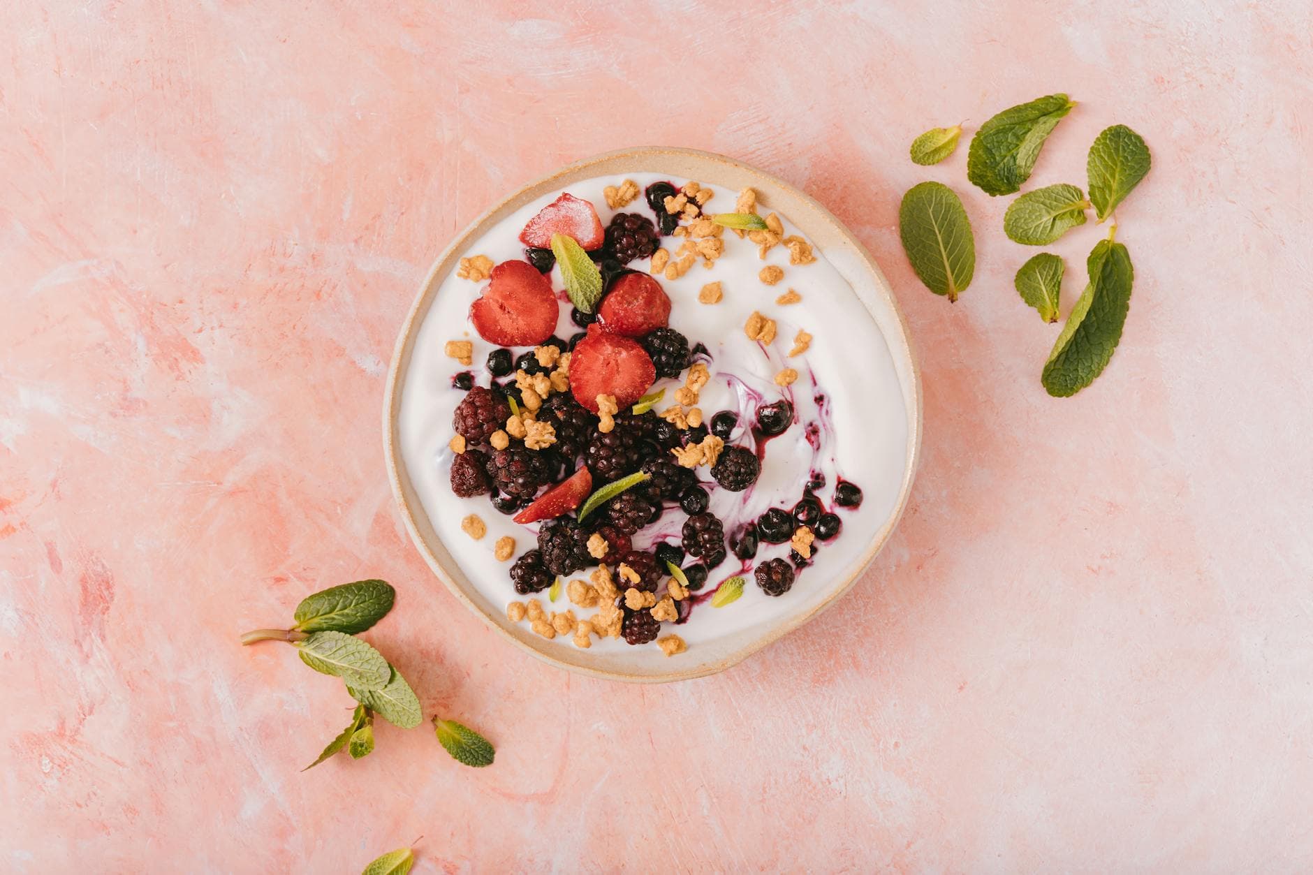 Top view of a vibrant yogurt bowl with mixed berries, granola, and mint leaves on a pink background. - probiotic recipes