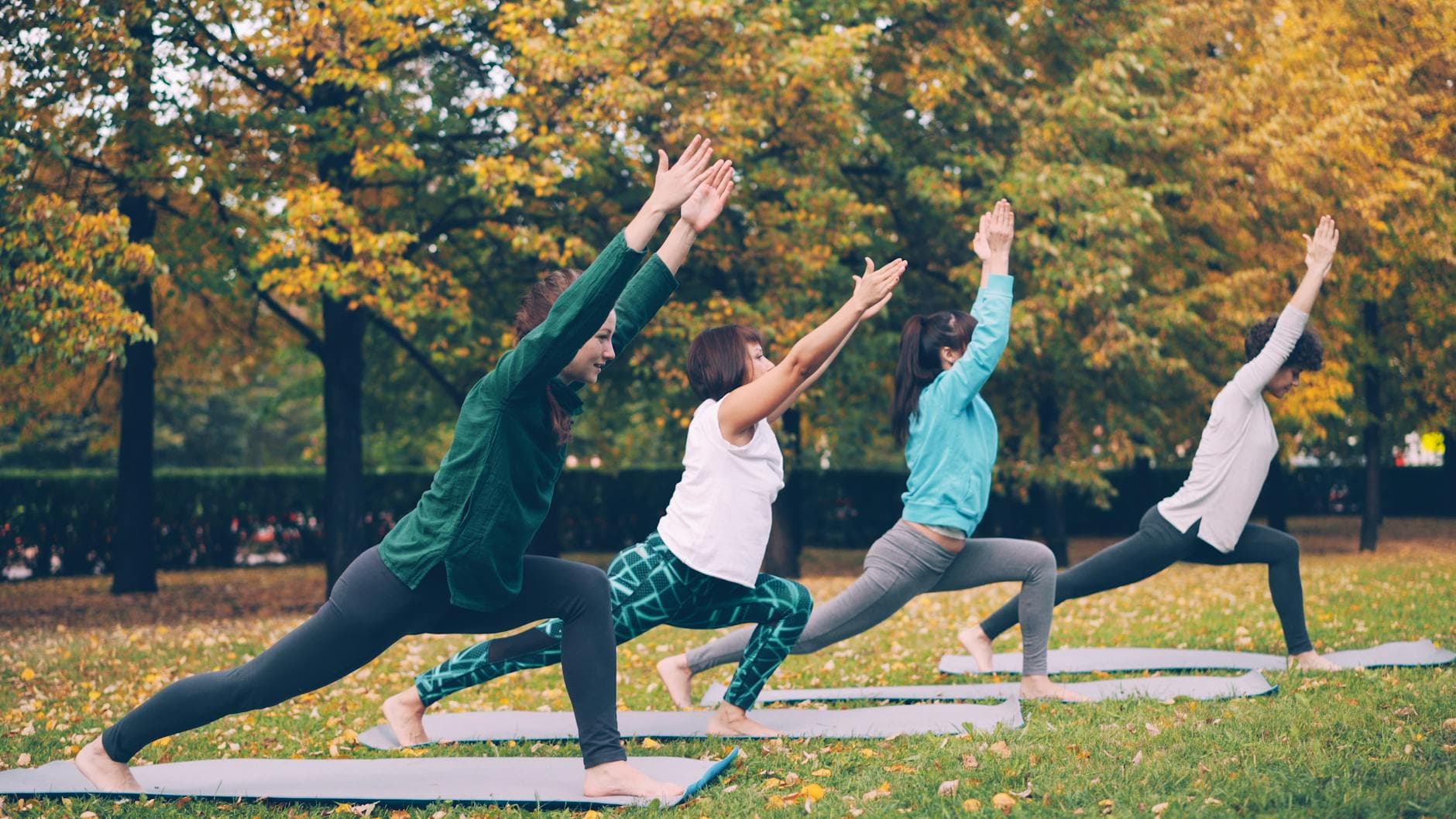 Four people practicing yoga outdoors surrounded by autumn foliage. - seasonal blues exercise