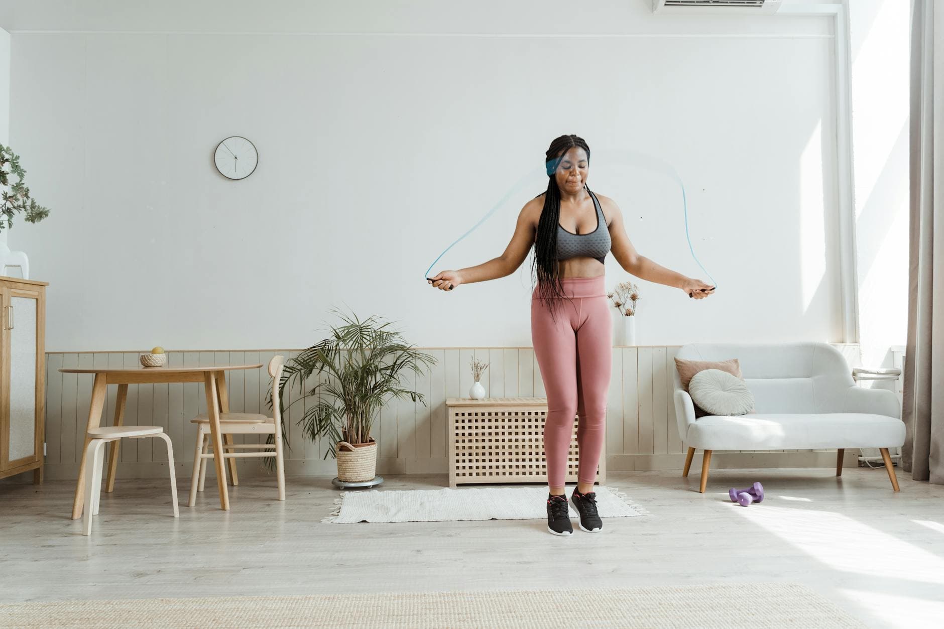 Confident black woman in activewear jump roping at home, promoting wellness and body positivity. - small space workouts
