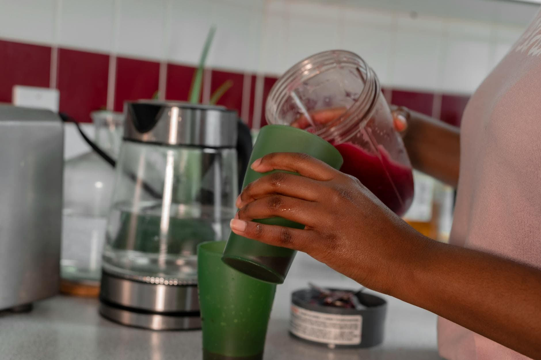 Close-up of a person pouring a healthy red smoothie into a green glass in a home kitchen. - spring energy smoothie