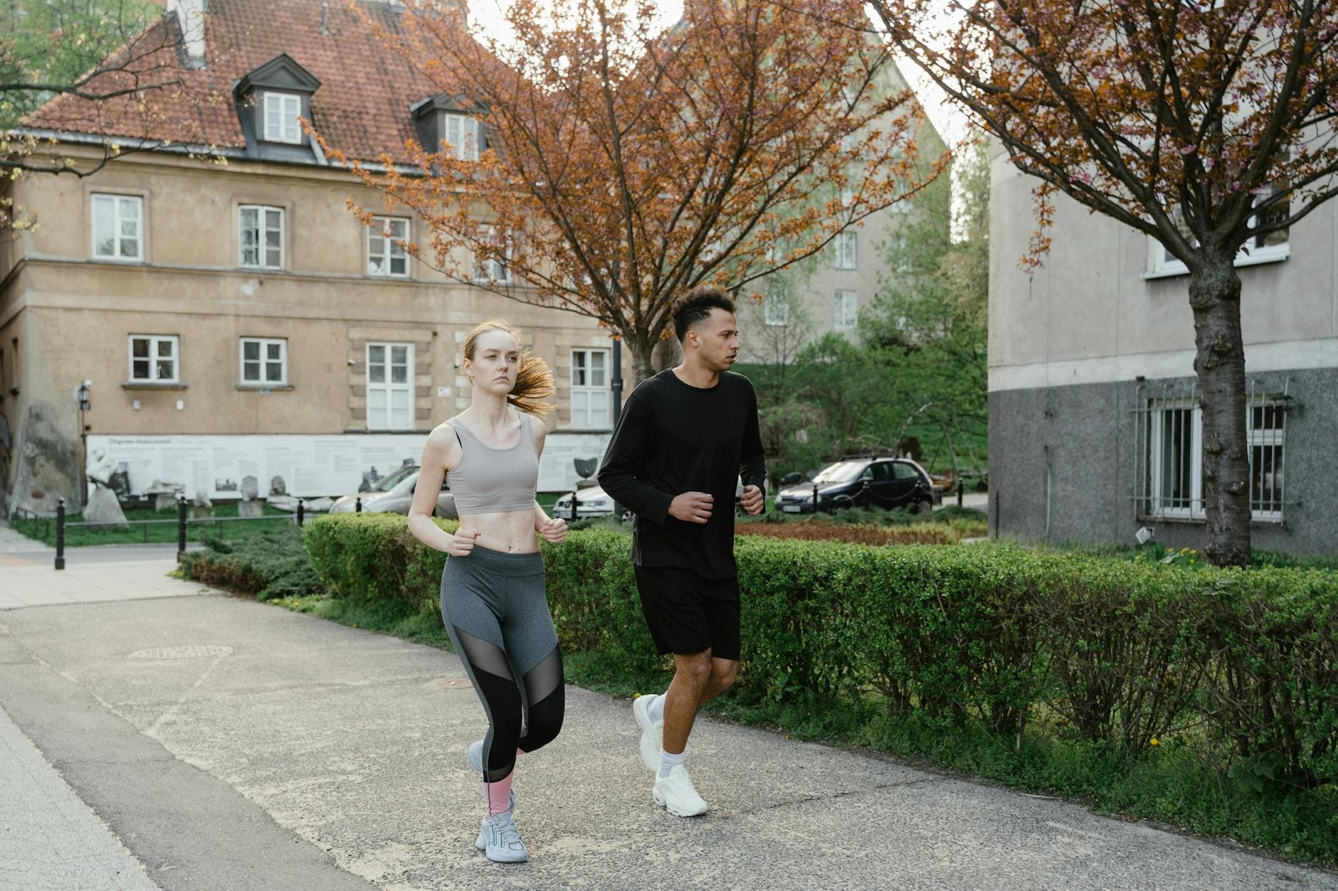 Two adults jogging on a sidewalk in an urban setting surrounded by spring foliage. - spring fitness goals