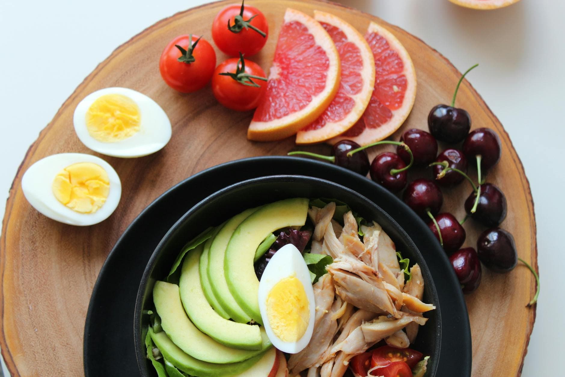 A vibrant, healthy salad bowl with avocado, eggs, tomatoes, grapefruit, and cherries on a wooden board. - spring nutrition macros