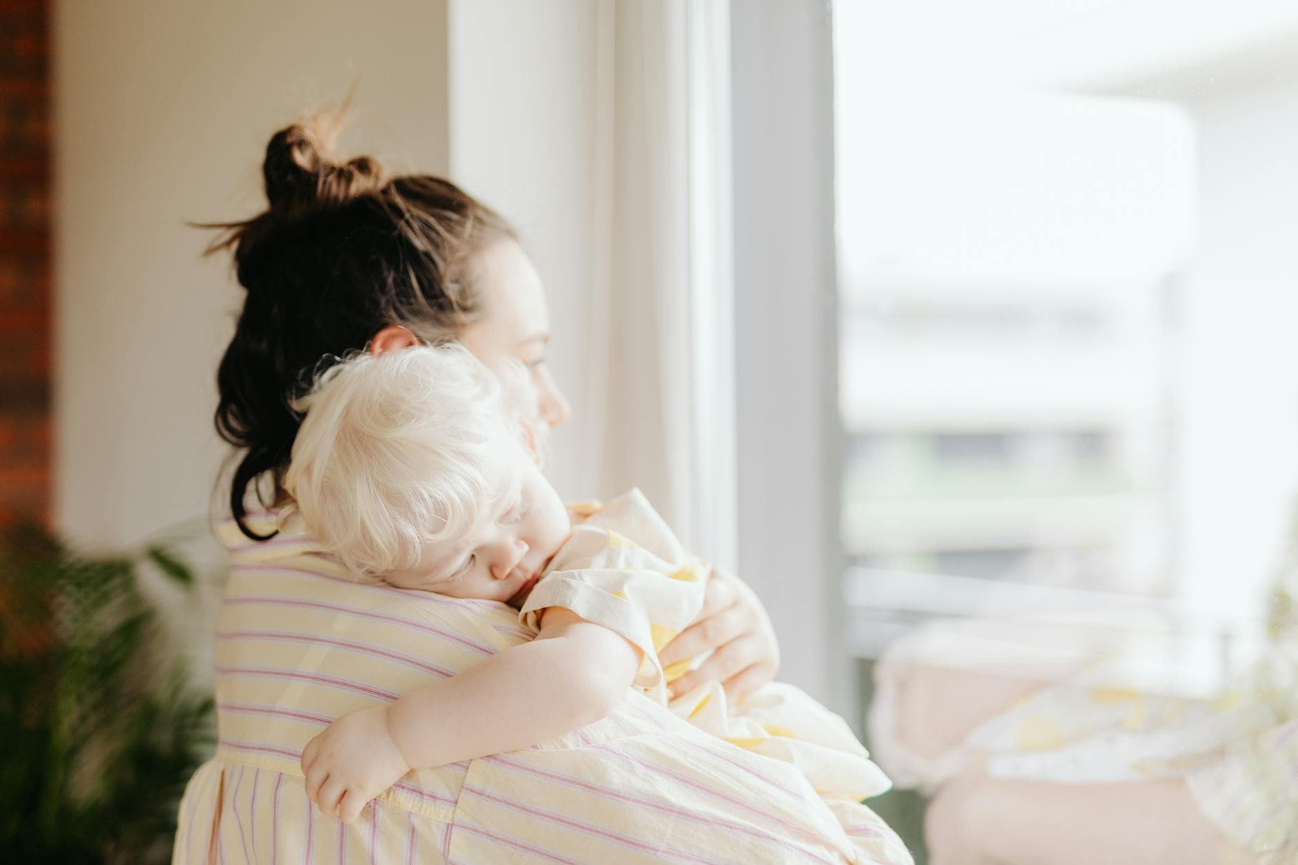 Peaceful moment of a mother holding her sleeping child indoors by a window. - spring sleep schedule