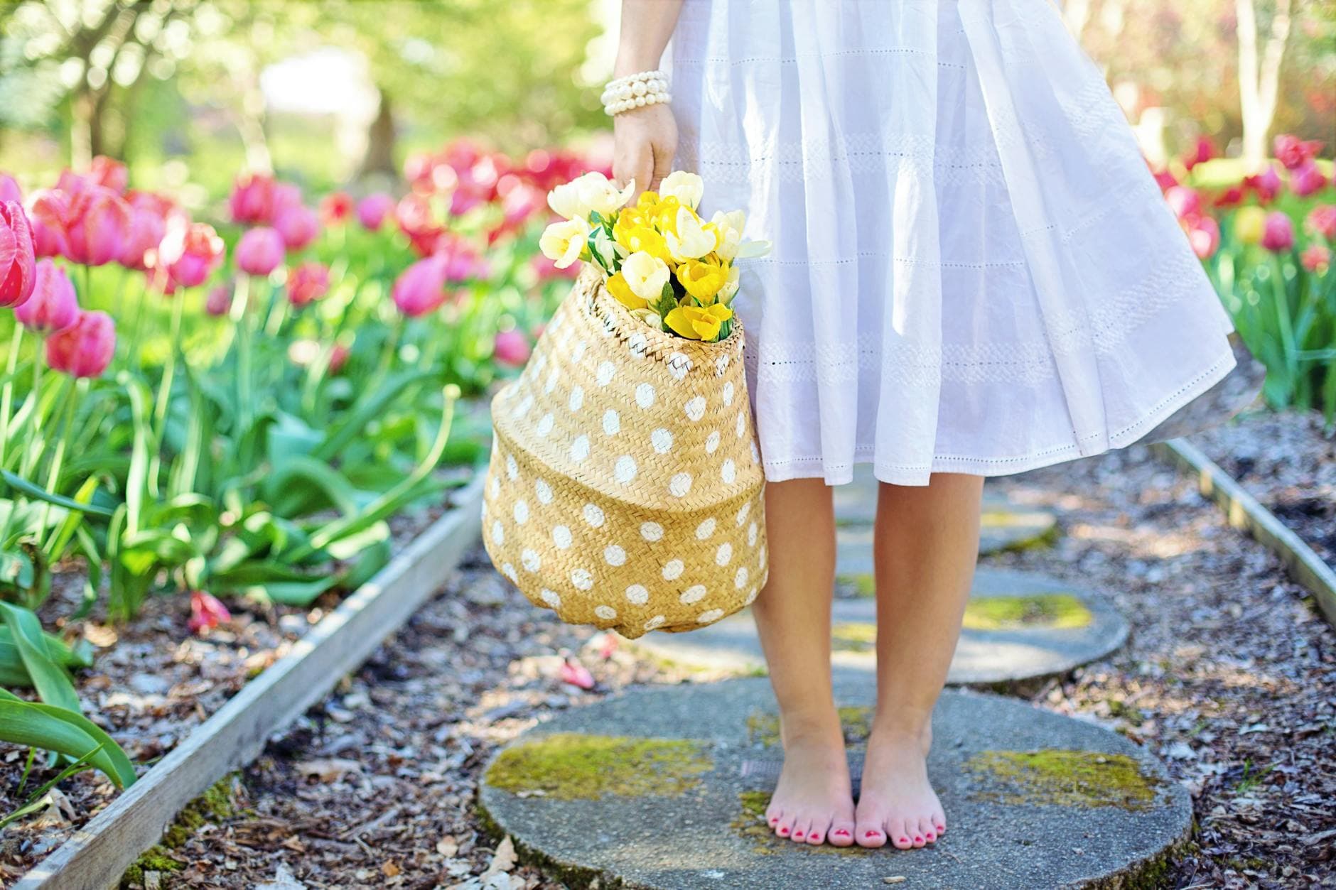 A woman in a white dress carries a basket of yellow flowers while walking barefoot in a tulip garden. - spring wellness reset