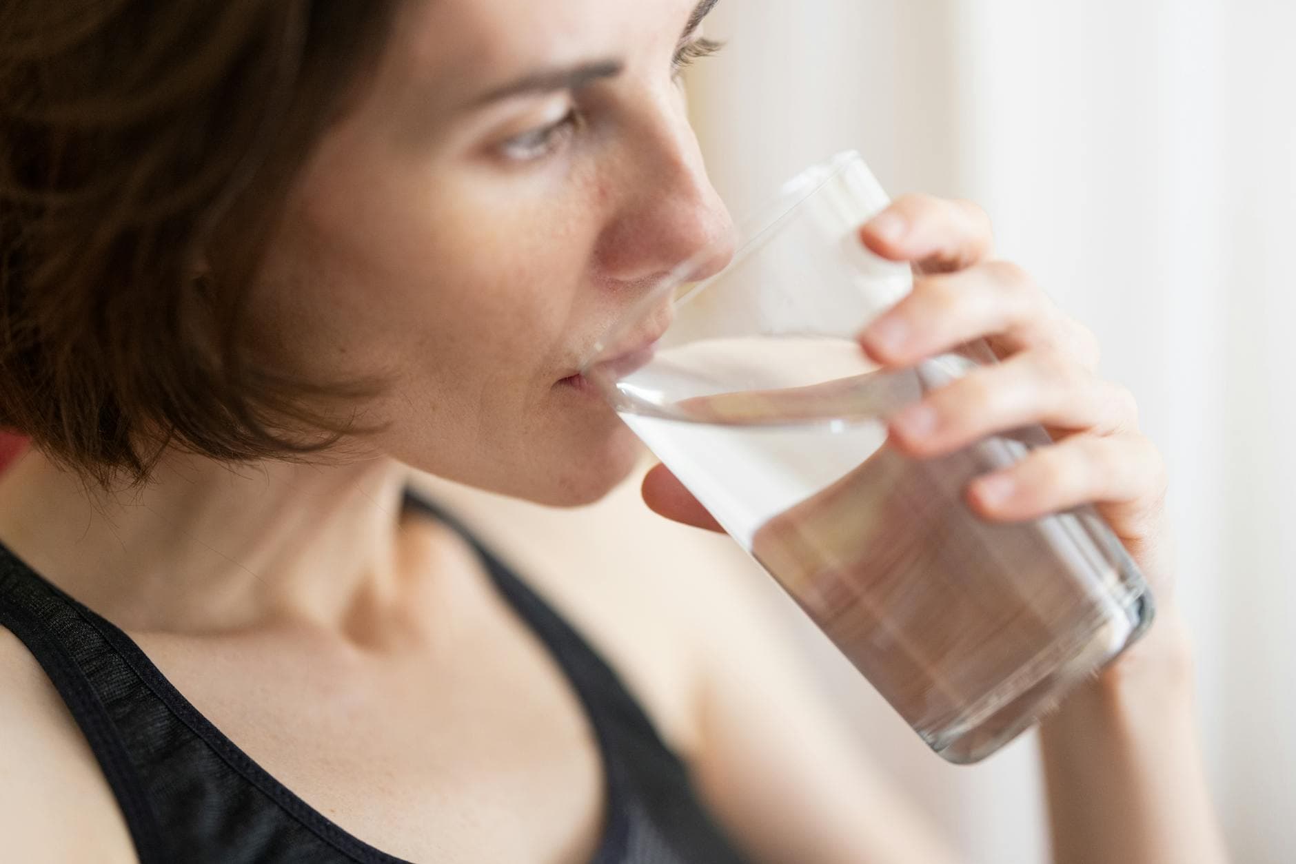 Close-up of an adult woman drinking a glass of water for hydration and health. - staying hydrated spring