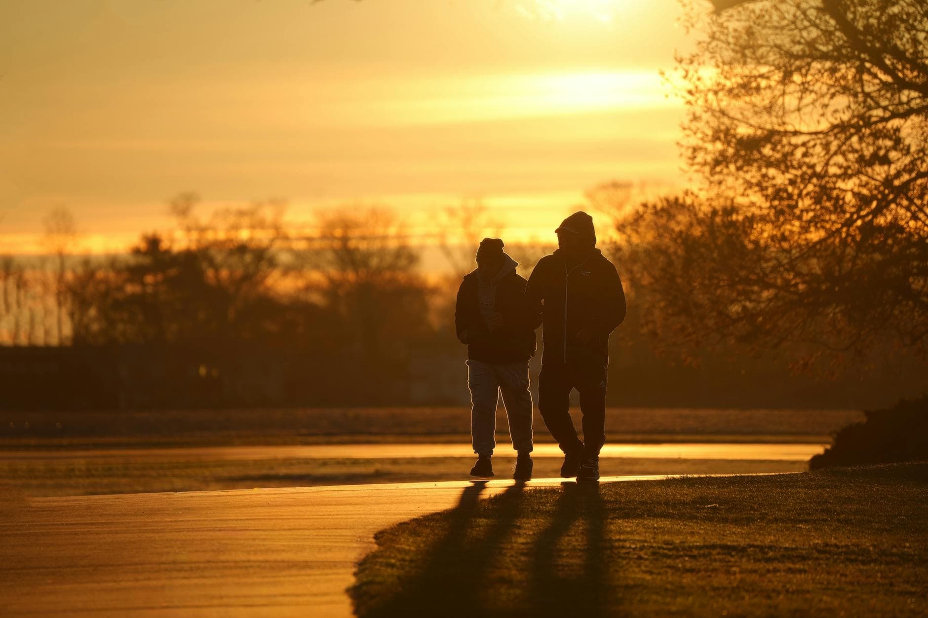 Silhouetted figures walking down a park path during a vivid sunrise. - sunrise workouts