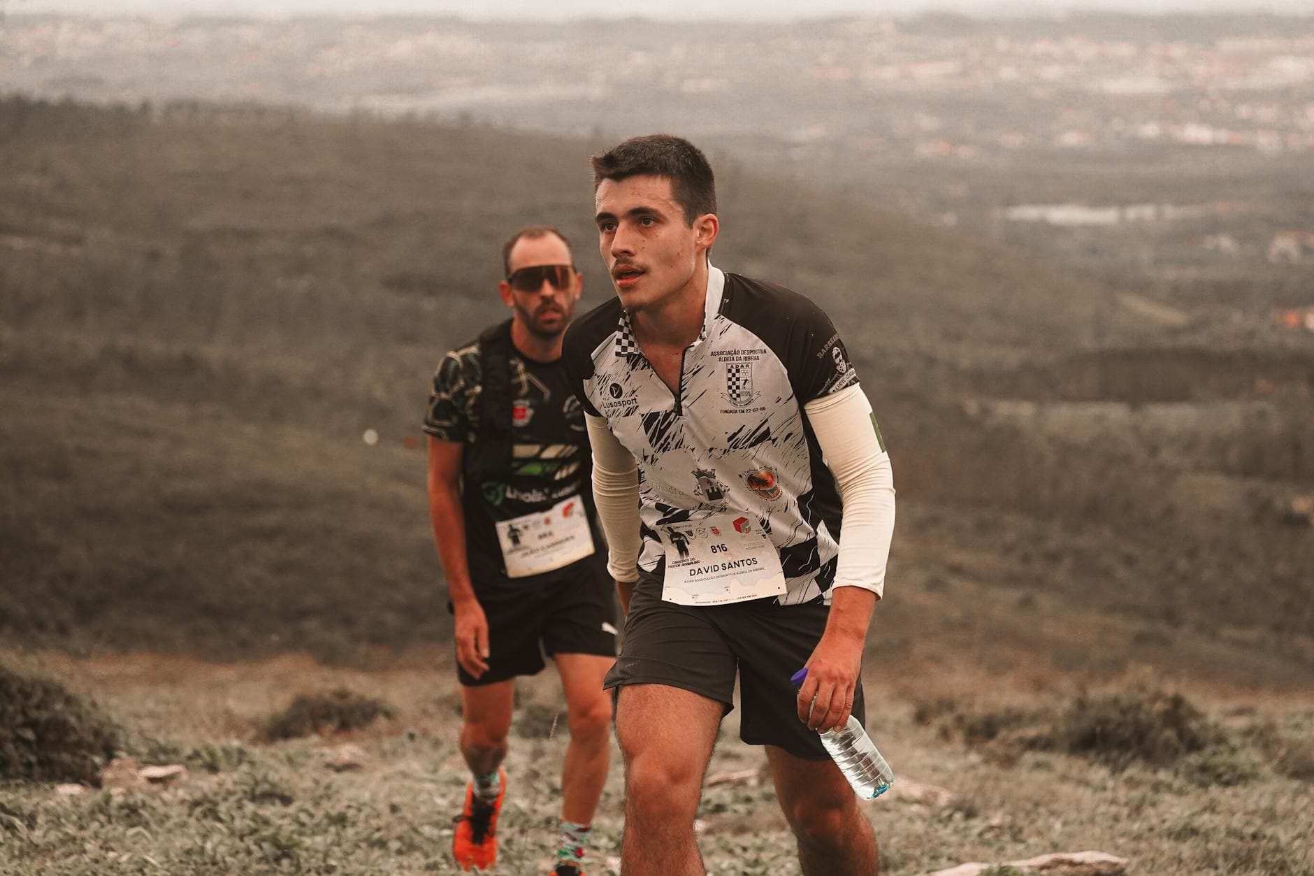 Two determined trail runners climbing a hillside during a marathon, showcasing endurance and scenic landscape. - trail running advanced