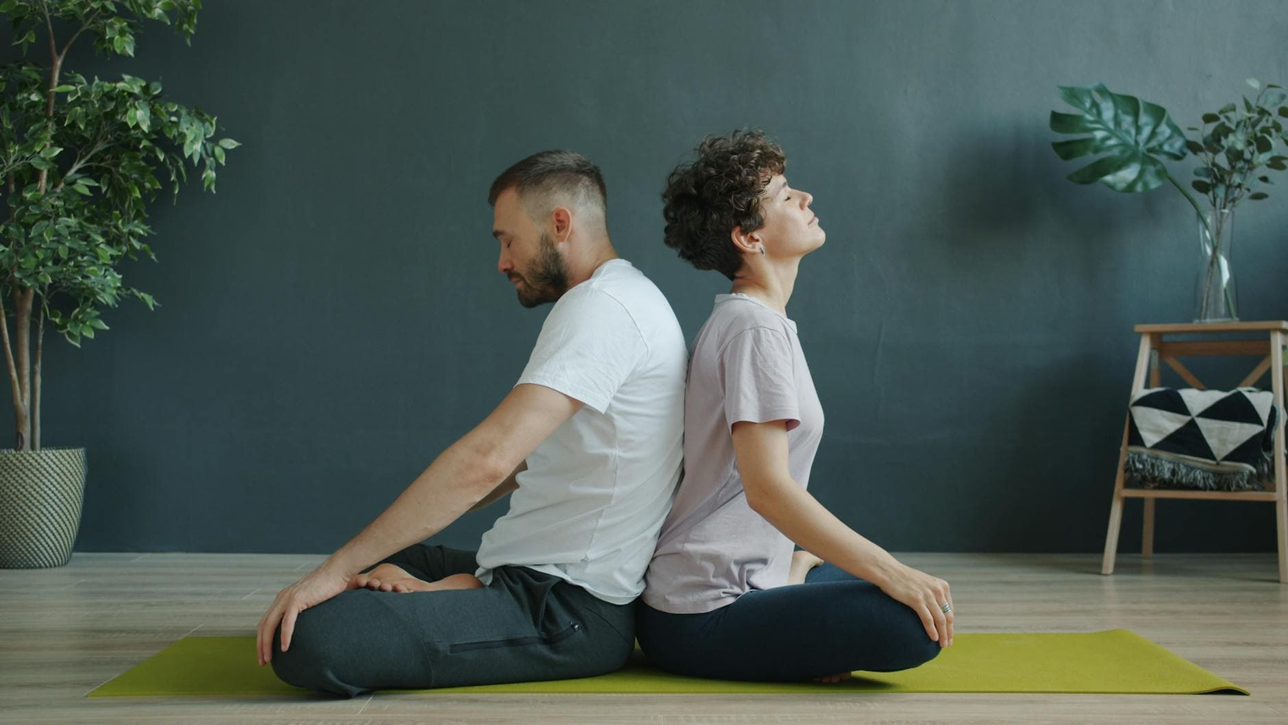 A couple meditating back to back on a yoga mat indoors, promoting relaxation and mindfulness. - yoga poses for beginners