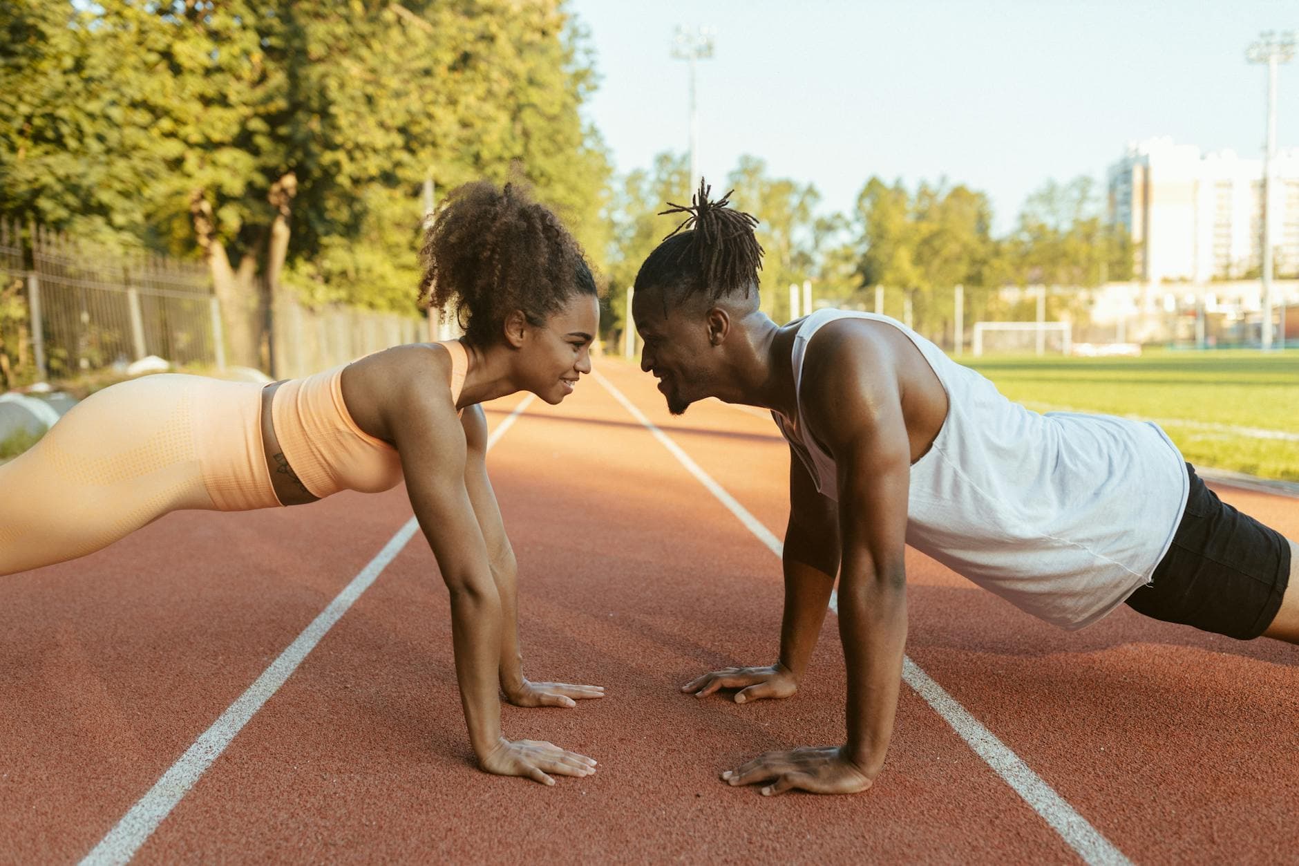 Fit couple performing push-ups together on an outdoor track under bright daylight. - best gold standard pre workout