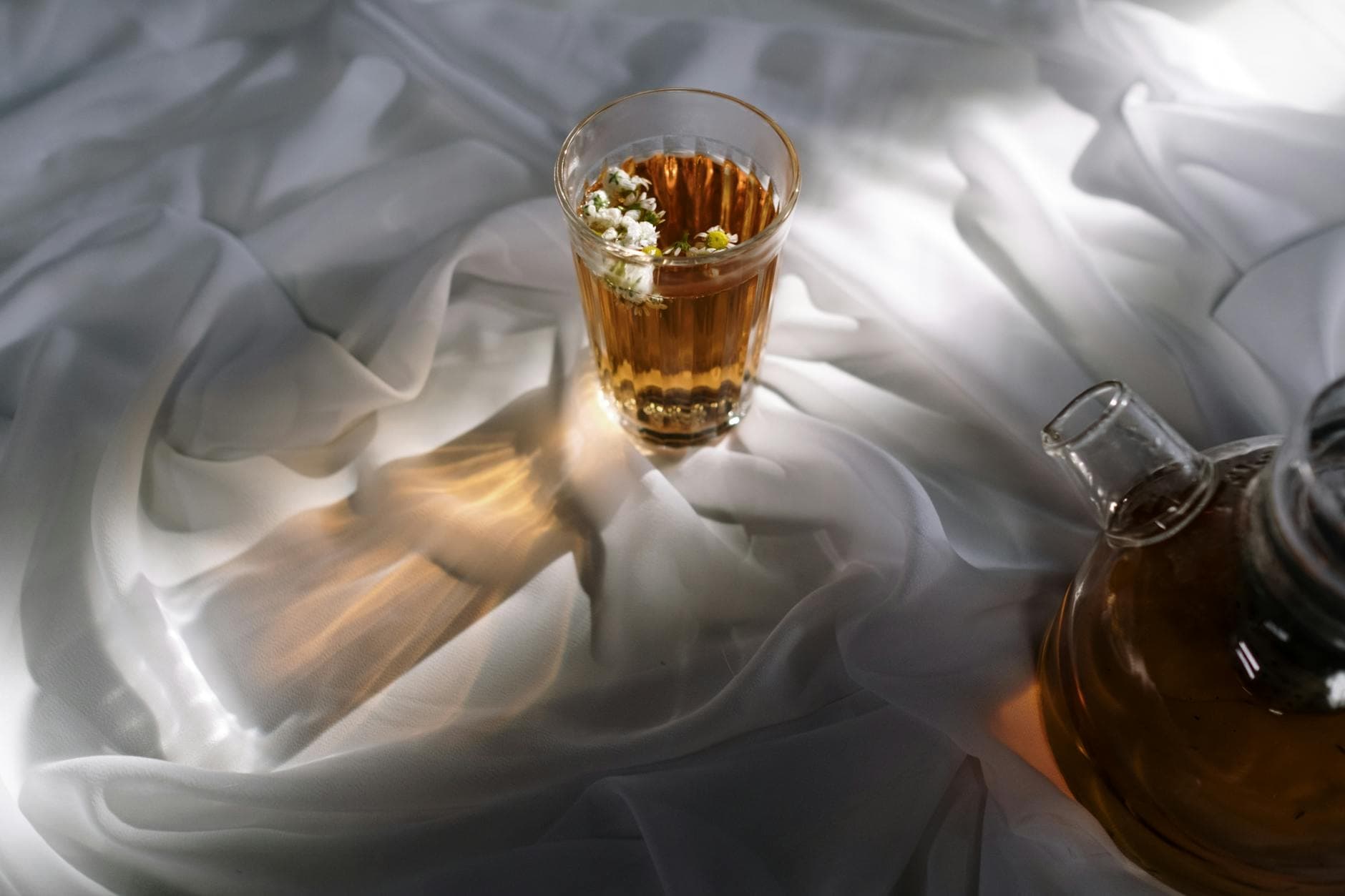 Glass of herbal tea with flowers on silky white fabric, beautifully lit. - bloating relief spring