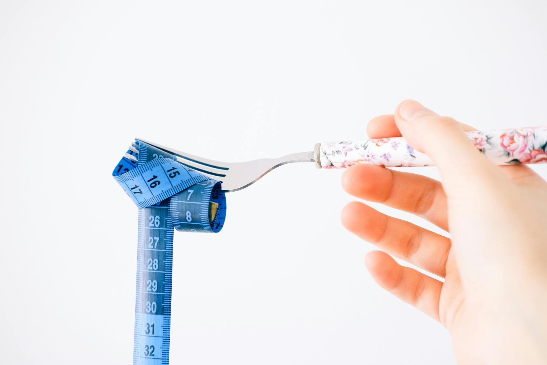 A floral-handled fork twirls a blue measuring tape, symbolizing diet and health. - boost metabolism fat loss