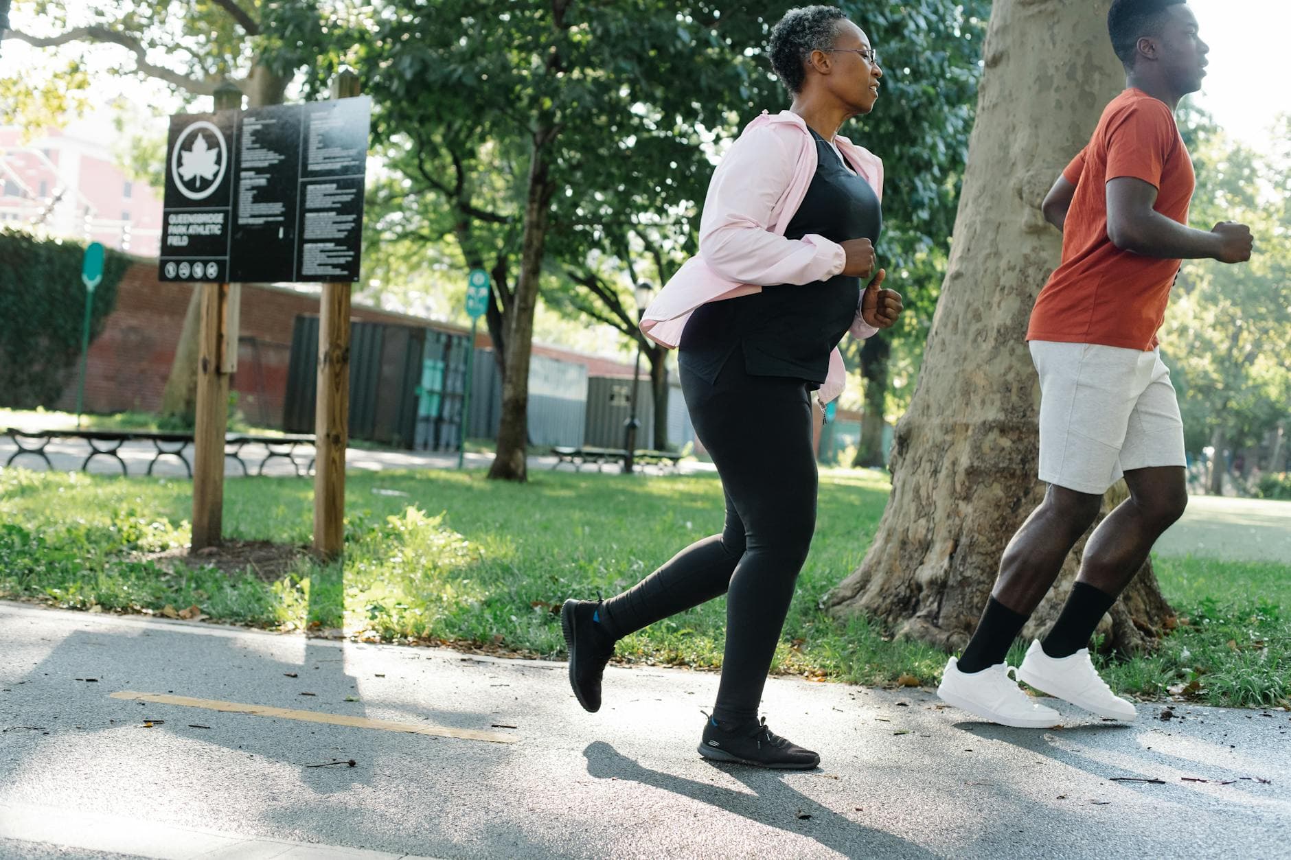 Two adults jogging on a sunny day in a green park, promoting fitness. - cardio for weight loss