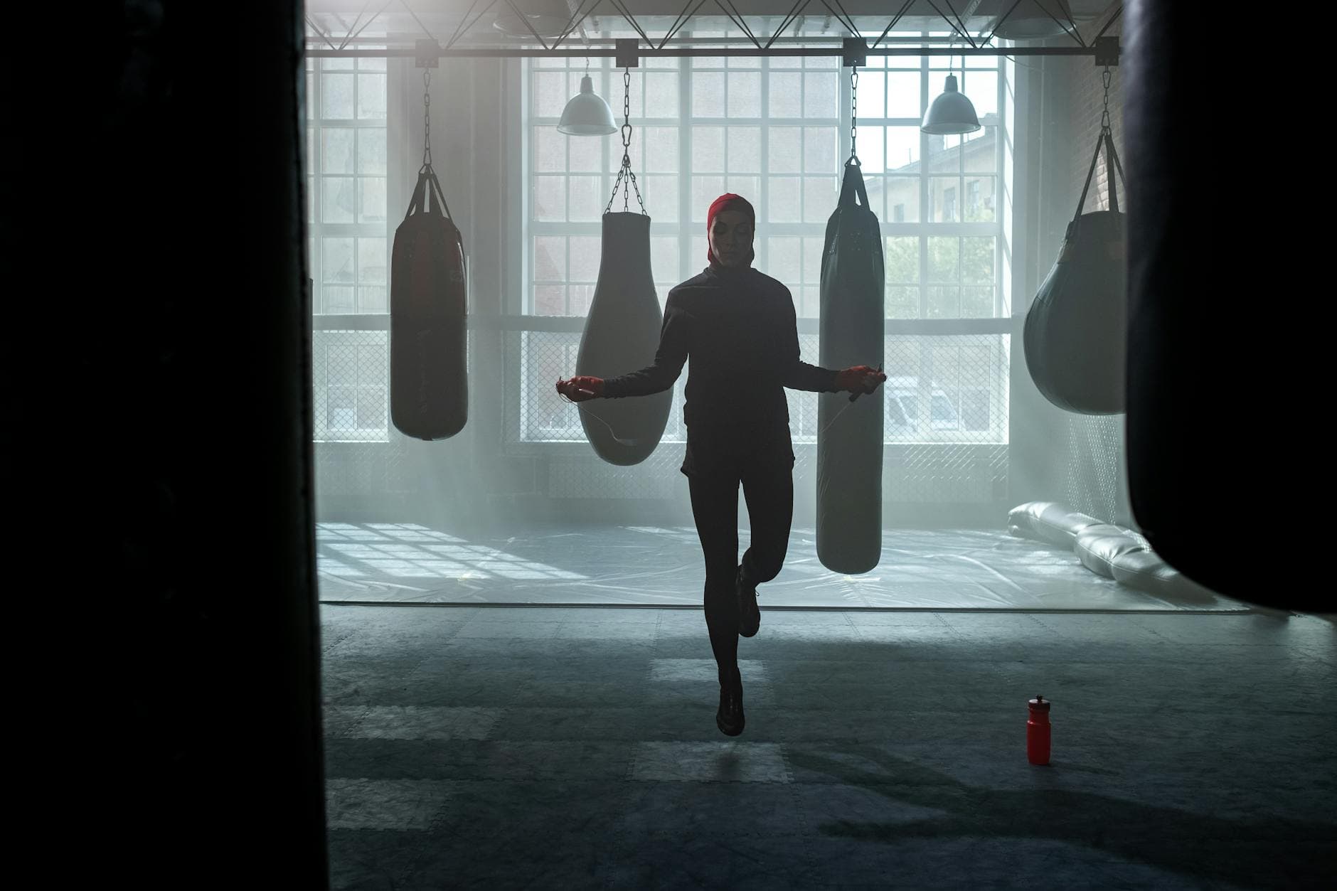 A woman exercises by jumping rope in a gym filled with punching bags. - may cardio workouts