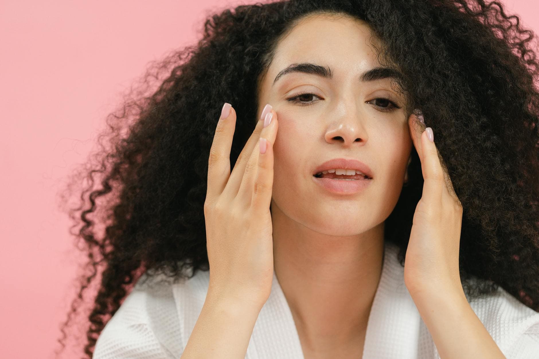A young woman with curly hair applies skincare products, emphasizing a healthy facial routine. - glowing skin recipes