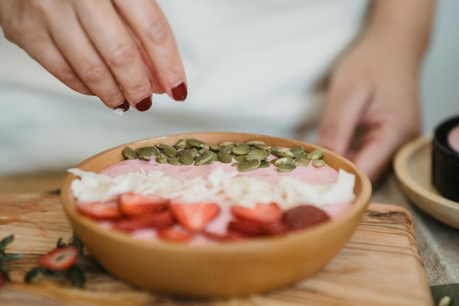 Hand garnishing a smoothie bowl with seeds, featuring strawberries and coconut flakes. - healthy smoothie recipes