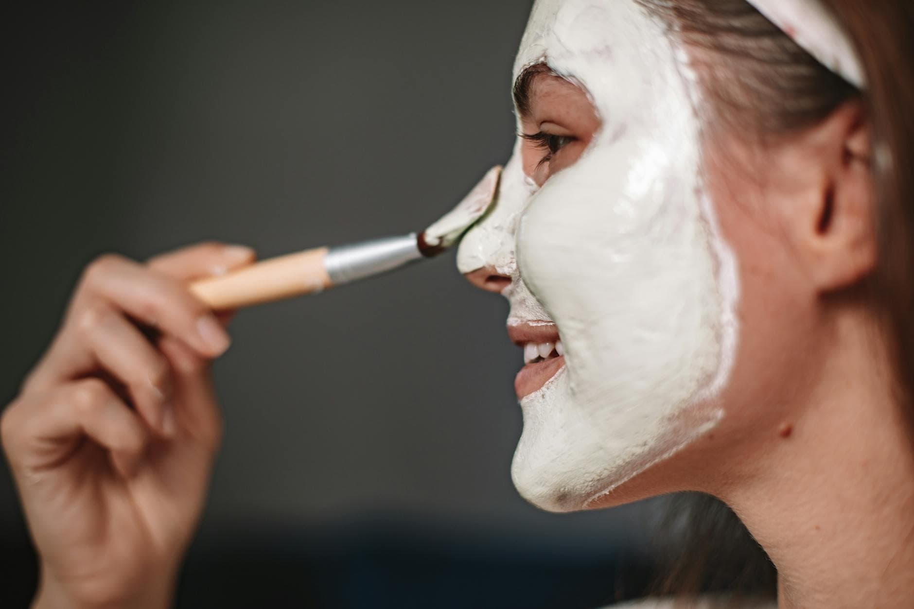 Smiling woman applying a facial mask with a brush, focusing on skincare and wellness. - hydrating recipes clear skin