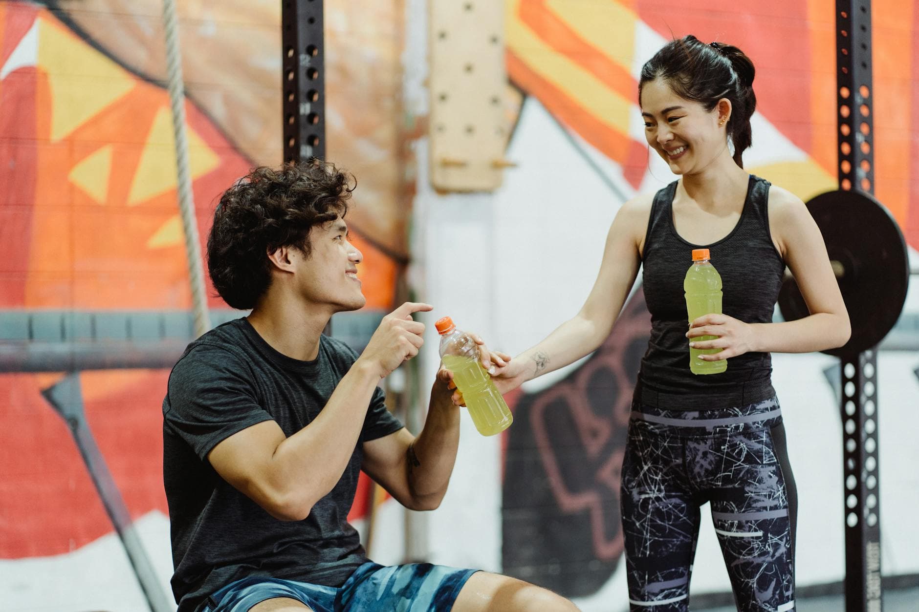 A man and woman sharing sports drinks in an energetic gym setting. - hydration for workouts