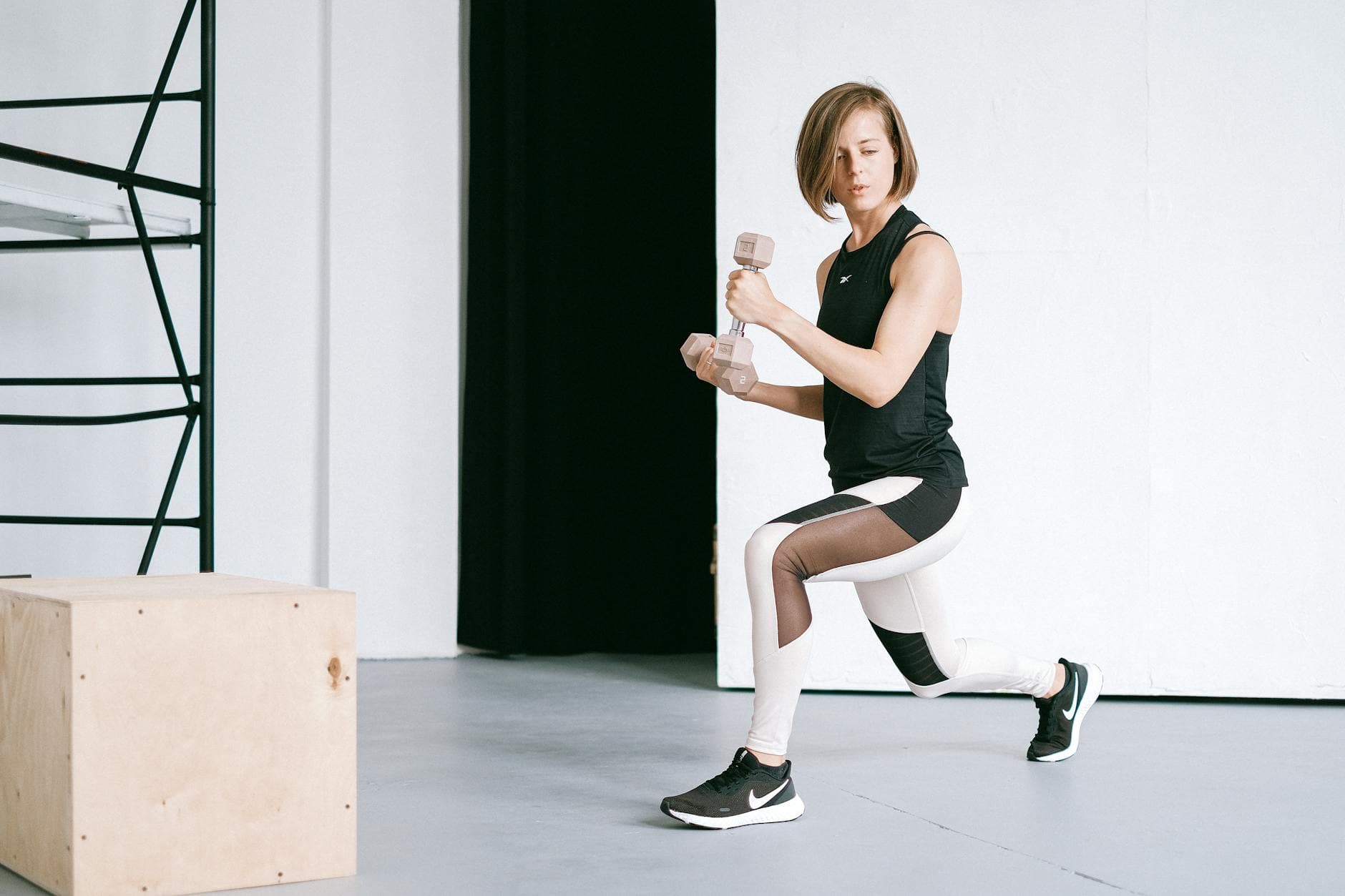 A young woman performing lunges with dumbbells in a modern indoor gym setting. - intermediate hiit workout