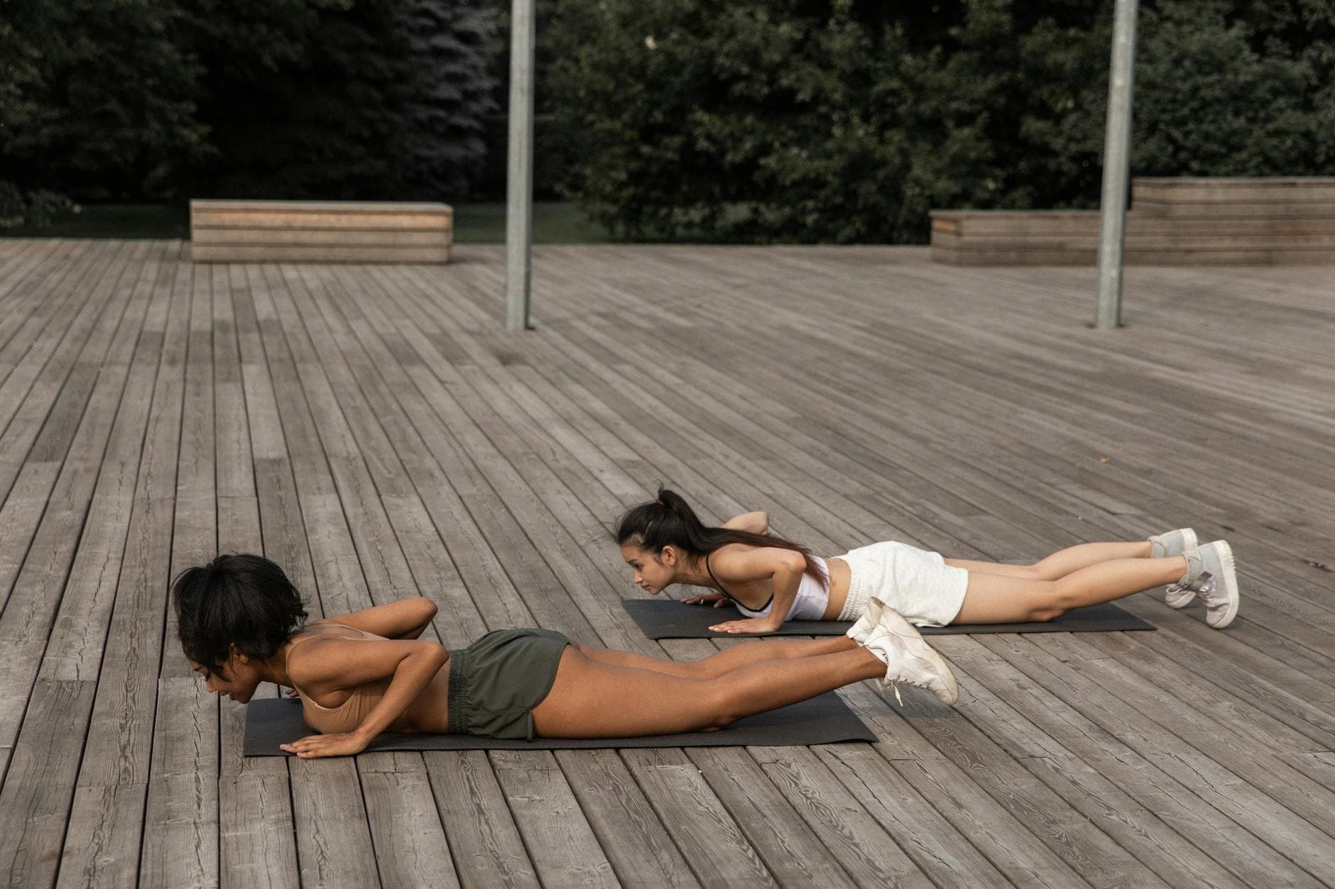 Side view of multiracial girlfriends in sportswear performing position on mats while practicing yoga in park - low impact spring workouts