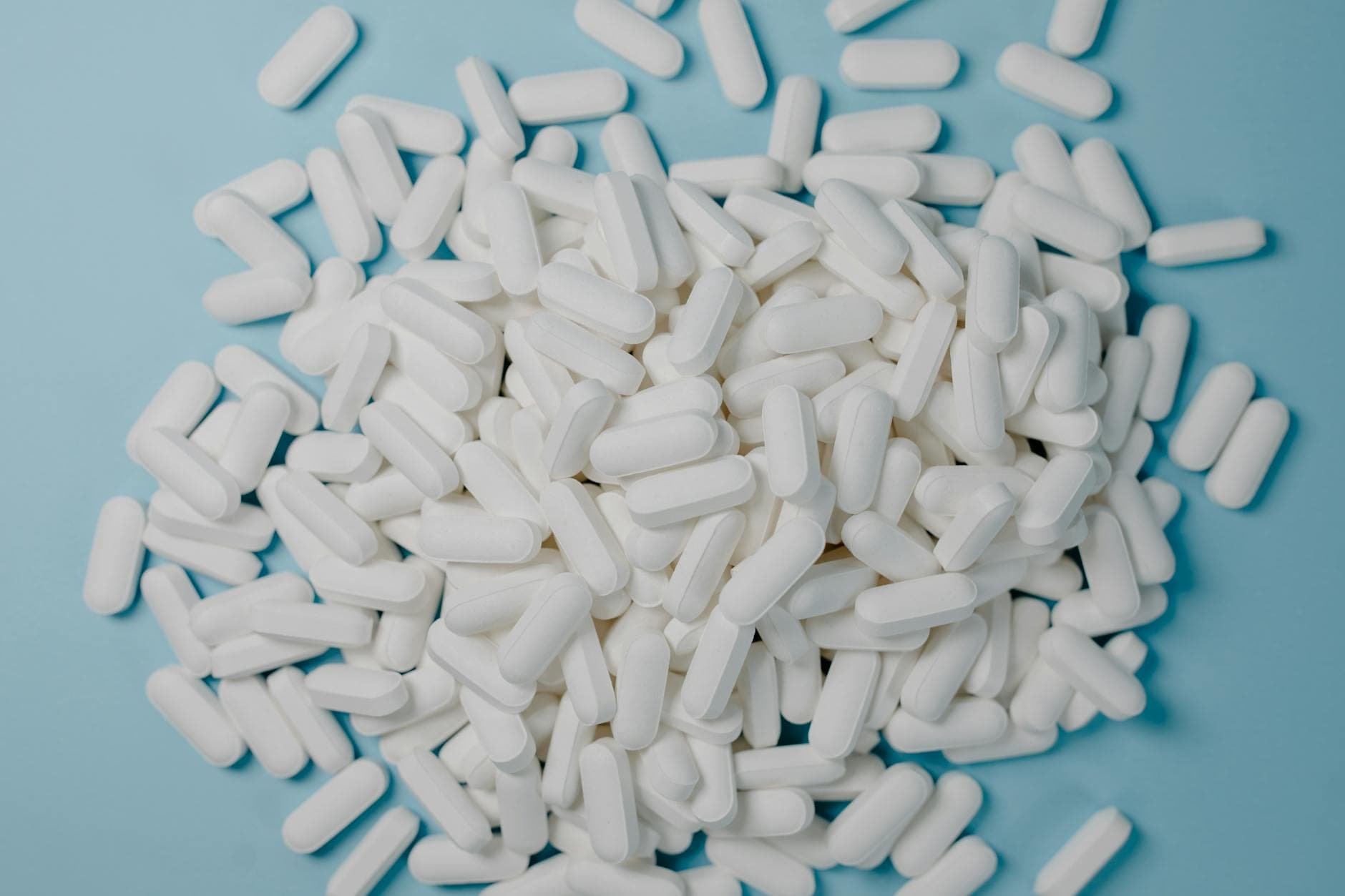 A collection of white oblong pills scattered on a blue surface, healthcare and medication concept. - probiotics gut health