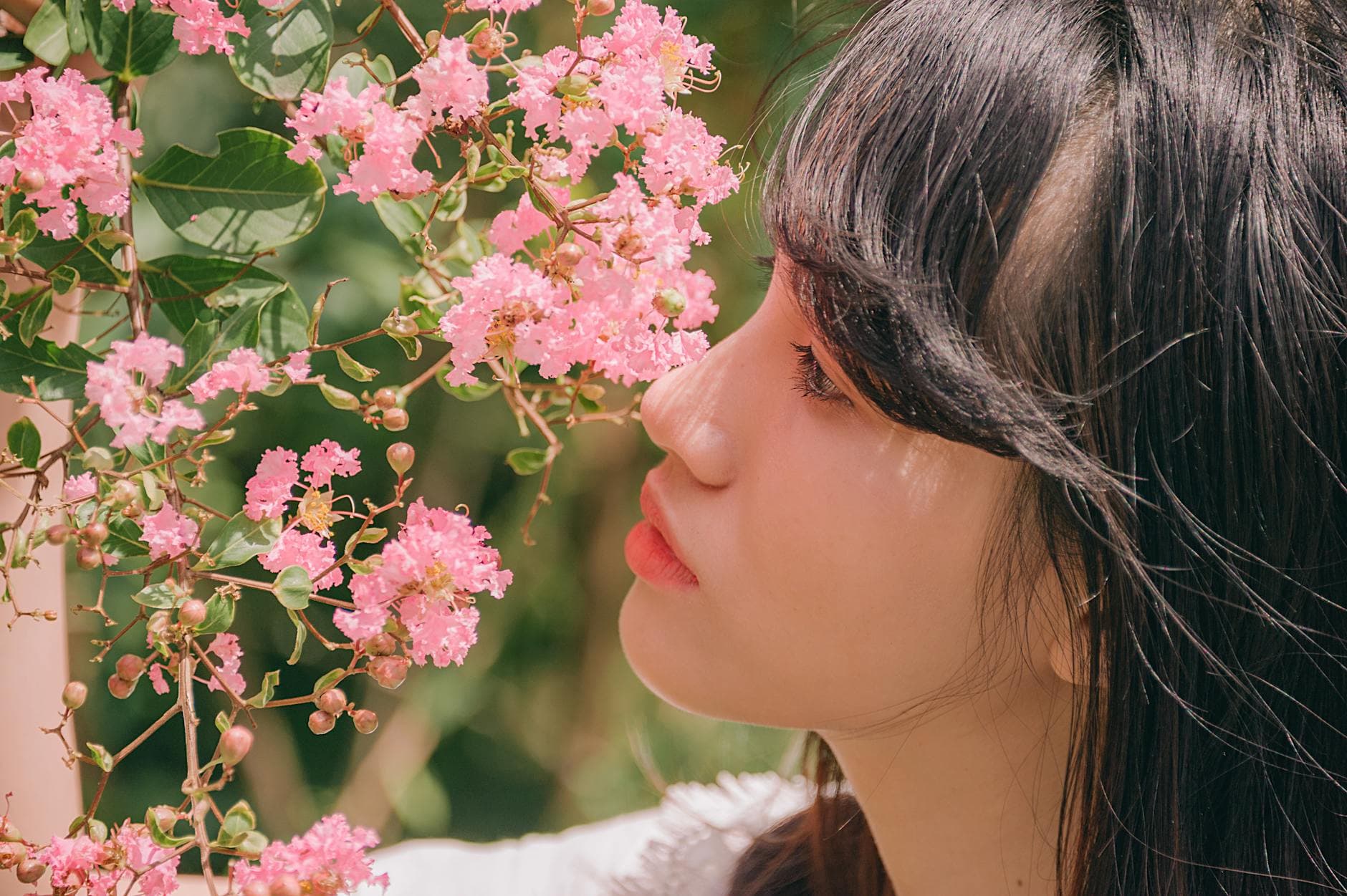 Asian woman enjoying the scent of vibrant pink blossoms outdoors. - spring allergy triggers