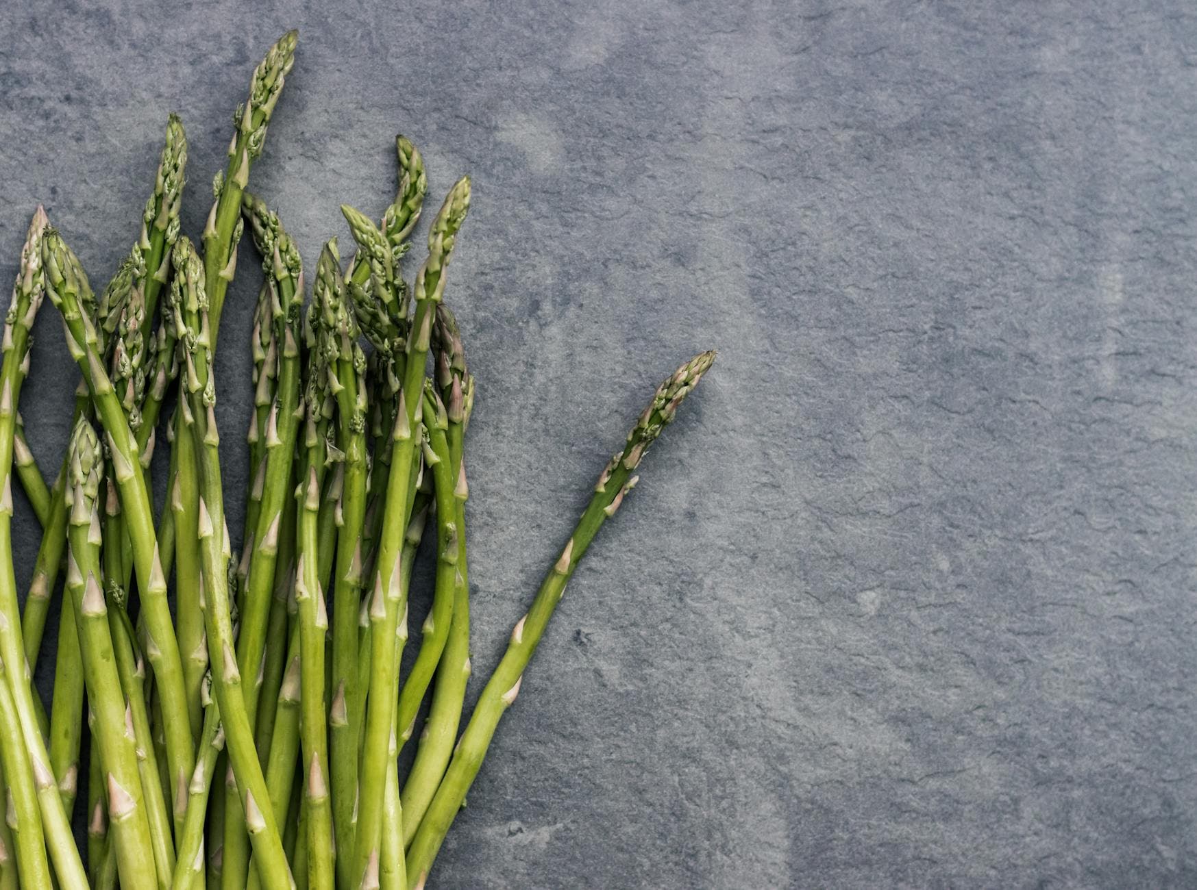 Close-up of fresh asparagus stalks on a textured slate background, perfect for health and food themes. - spring detox cleanse