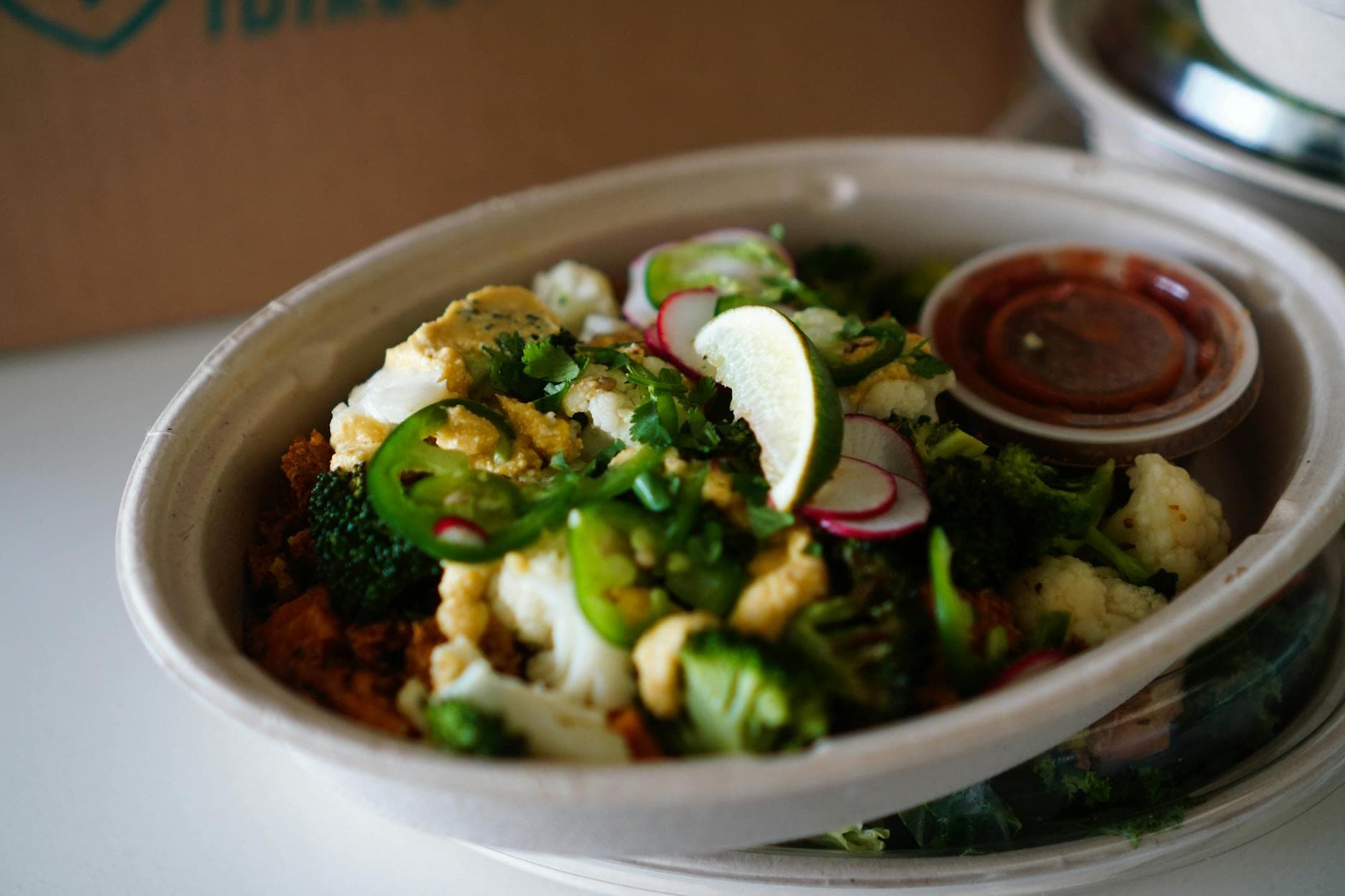 Colorful vegetable salad bowl with broccoli, cauliflower, jalapeno, and lime in eco-friendly packaging. - spring energy lunch