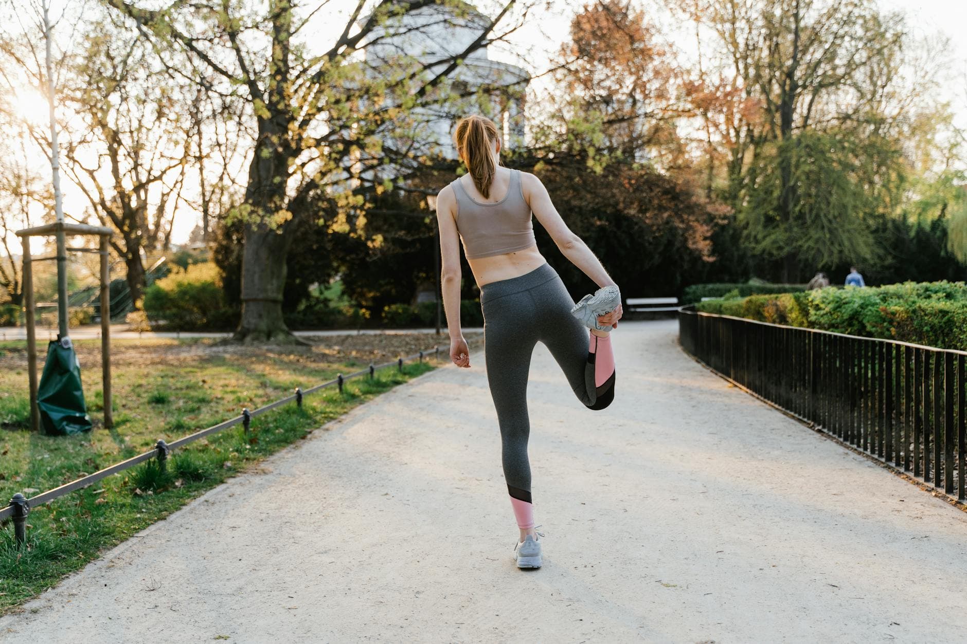 A woman performs a stretching exercise in a park setting, showcasing fitness and a healthy lifestyle. - spring exercise daylight