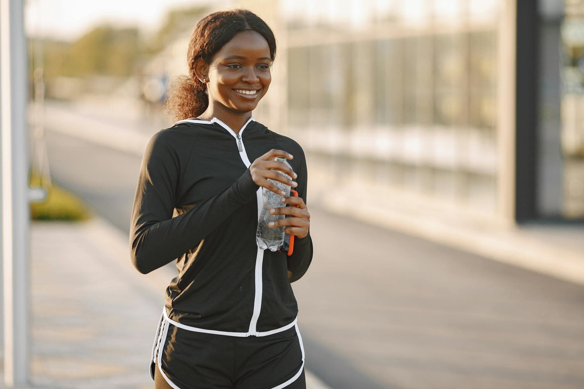 Smiling woman in activewear holding a water bottle outdoors during daytime. - spring hike hydration